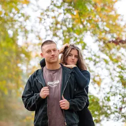 Porträt eines jungen Paares in entspannter Pose vor einem unscharfen Hintergrund aus herbstlichem Laubwerk im Freien