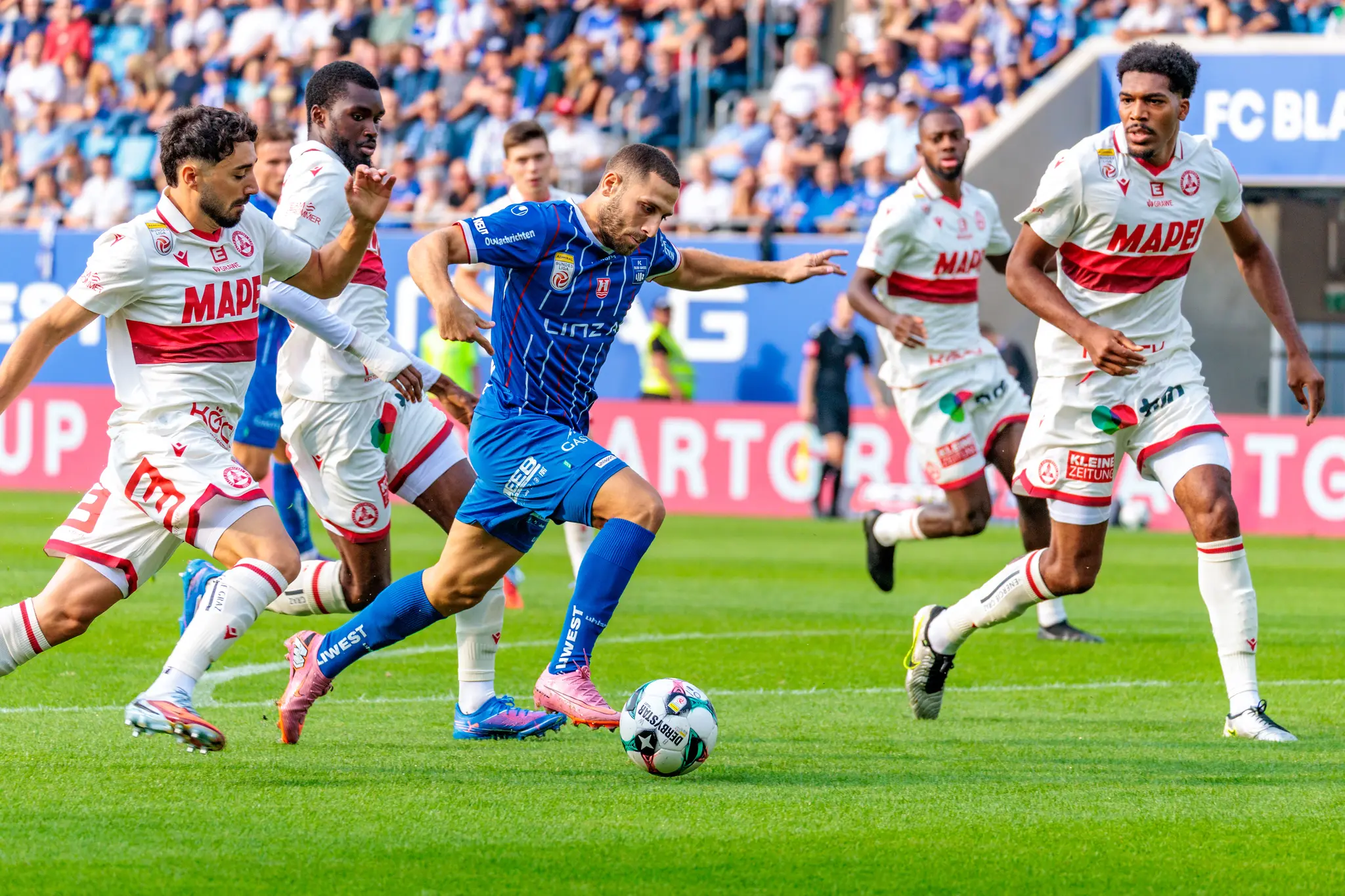 Der Stürmer von Blau-Weiß Linz, Shon Weissman, dribbelt im Bundesliga-Spiel dynamisch am Ball, bedrängt von mehreren Verteidigern des GAK