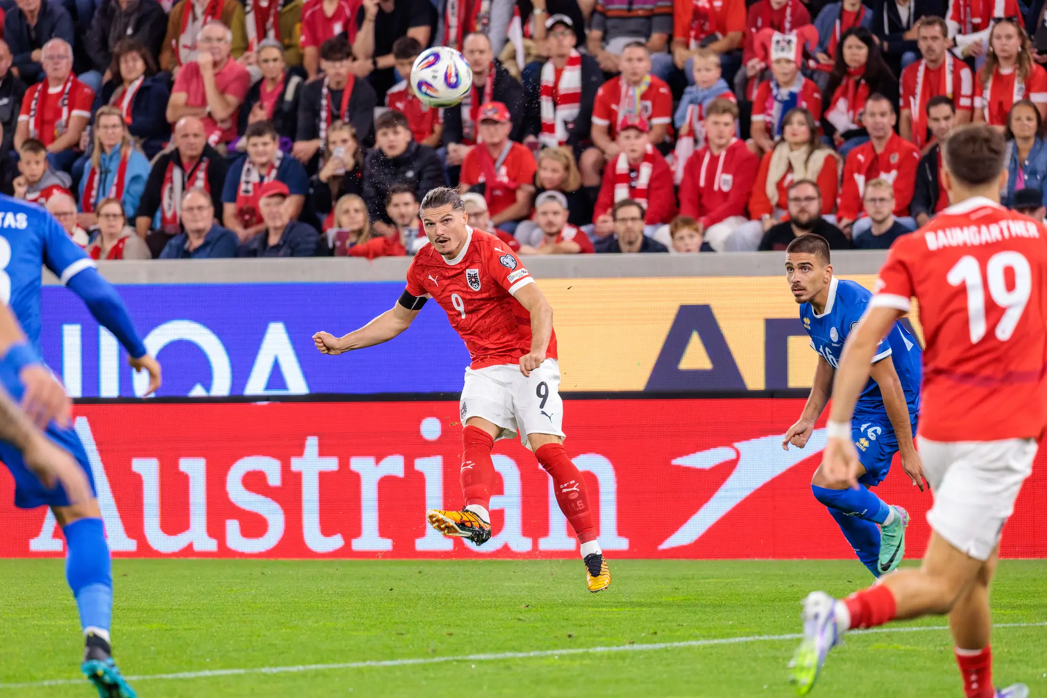 Der österreichische Nationalspieler Marcel Sabitzer im roten Trikot mit der Rückennummer 9 tritt im Sprung einen Fußball während eines Länderspiels gegen Zypern, im Hintergrund sind die jubelnden Fans zu sehen