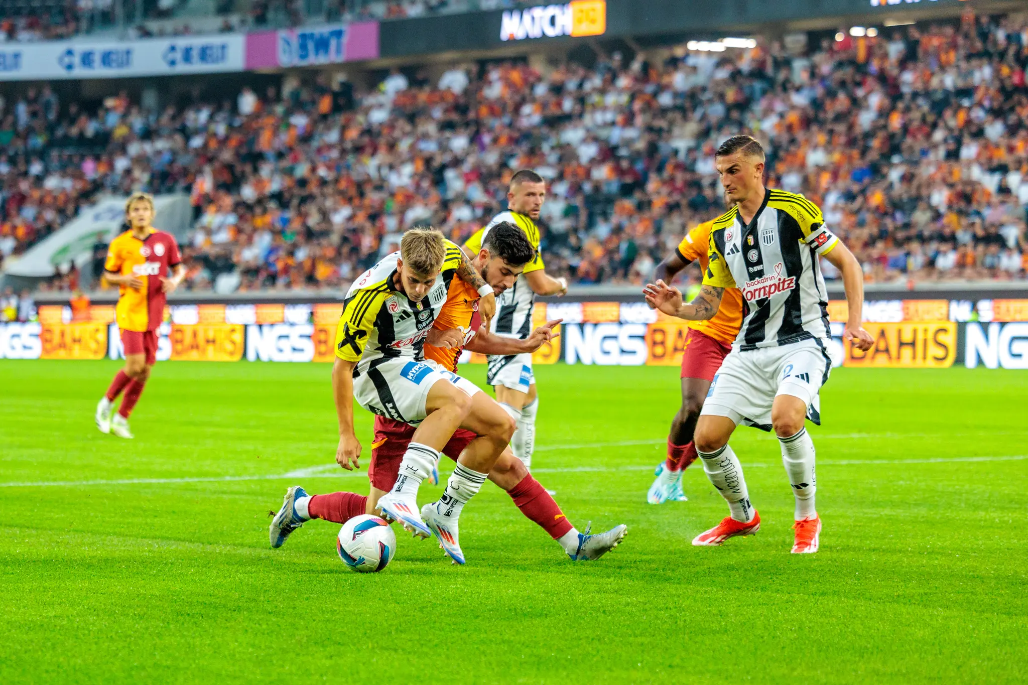 Ein Fußballspieler des LASK im schwarz-weiß gestreiften Trikot kämpft mit einem Spieler von Galatasaray im orange-roten Trikot um den Ball in der Raiffeisen Arena bei einem Vorbereitungsspiel im Rahmen der Nero Summer Series 2024 