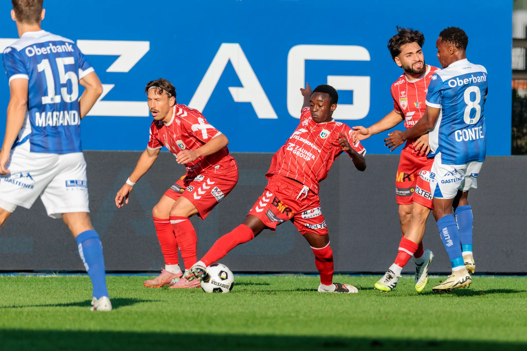 Manuel Maranda und Karim Conte vom FC Blau-Weiß Linz stellen sich im Mittelfeld drei Welsern entgegen, der Ball liegt am Fuß eines Angreifers; im Hintergrund leuchtet die Linz-AG-Bande.