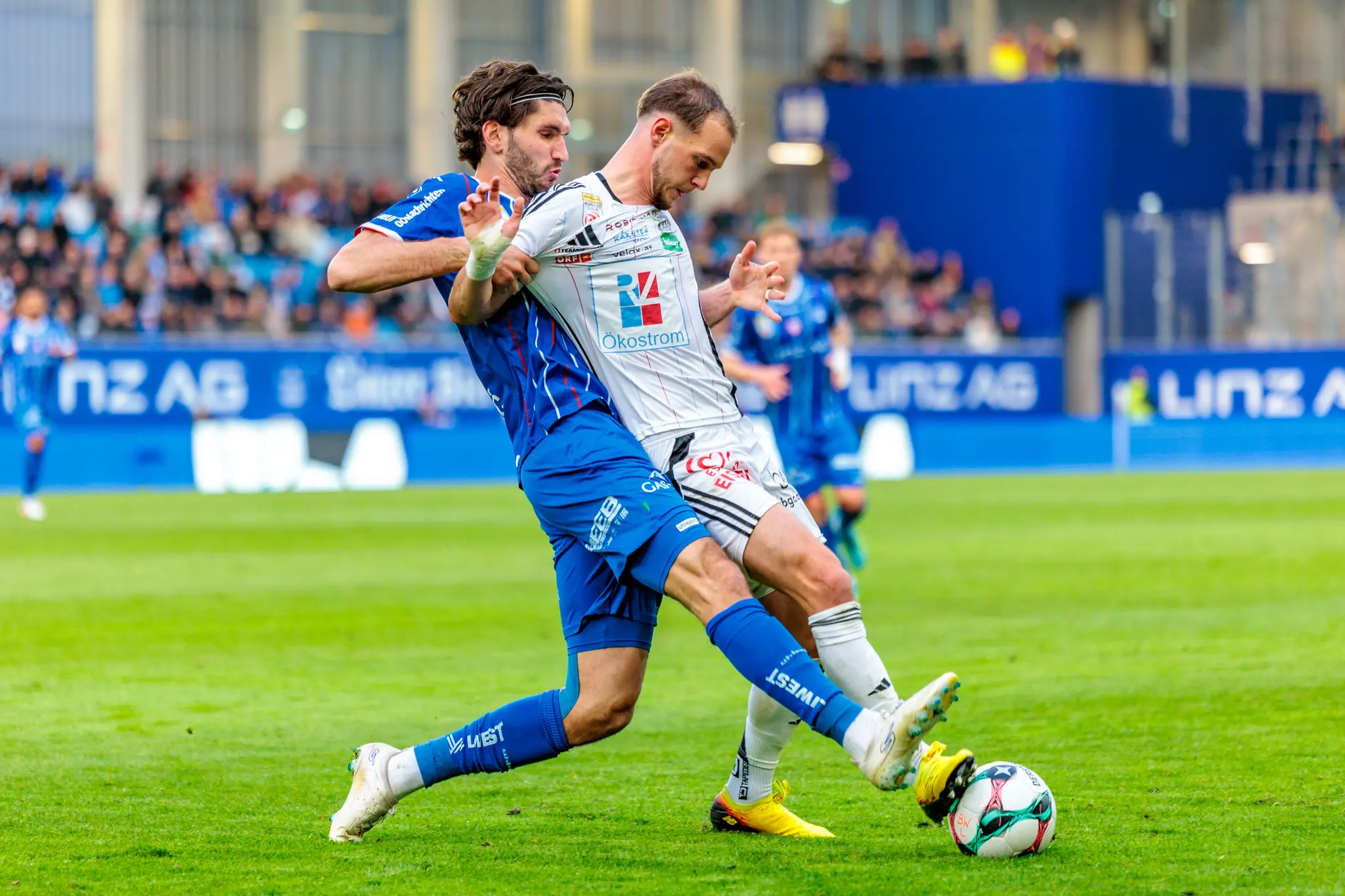 Ein Spieler von Blau-Weiß Linz und ein Spieler des Wolfsberger AC führen einen intensiven Zweikampf um den Ball aus