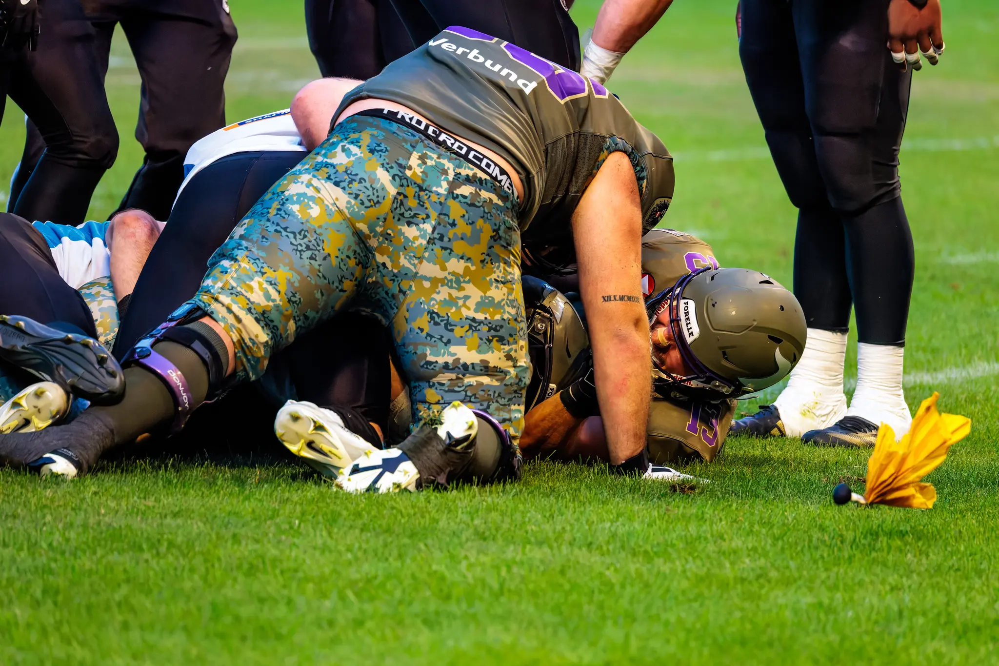 Nach dem Tackling von Karri Pajarinen (Nummer 24) liegen mehrere Spieler am Boden, eine gelbe Straf-Flagge liegt auf dem Spielfeld.