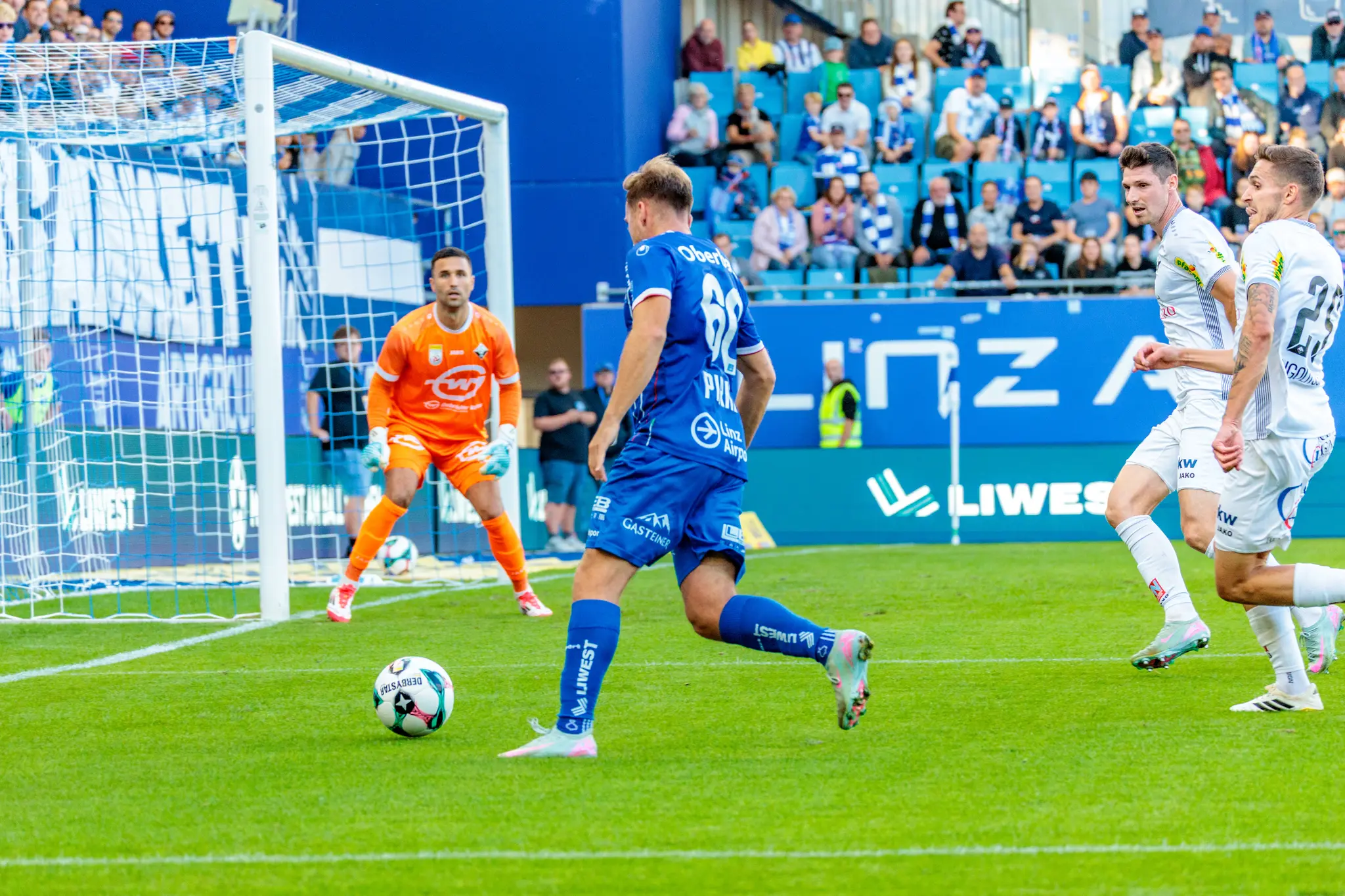 Der Fußballspieler Paul Mensah vom FC Blau-Weiß Linz schießt den Ball in Richtung des Tores, das von Altach-Tormann Dejan Stojanovic in Orange verteidigt wird