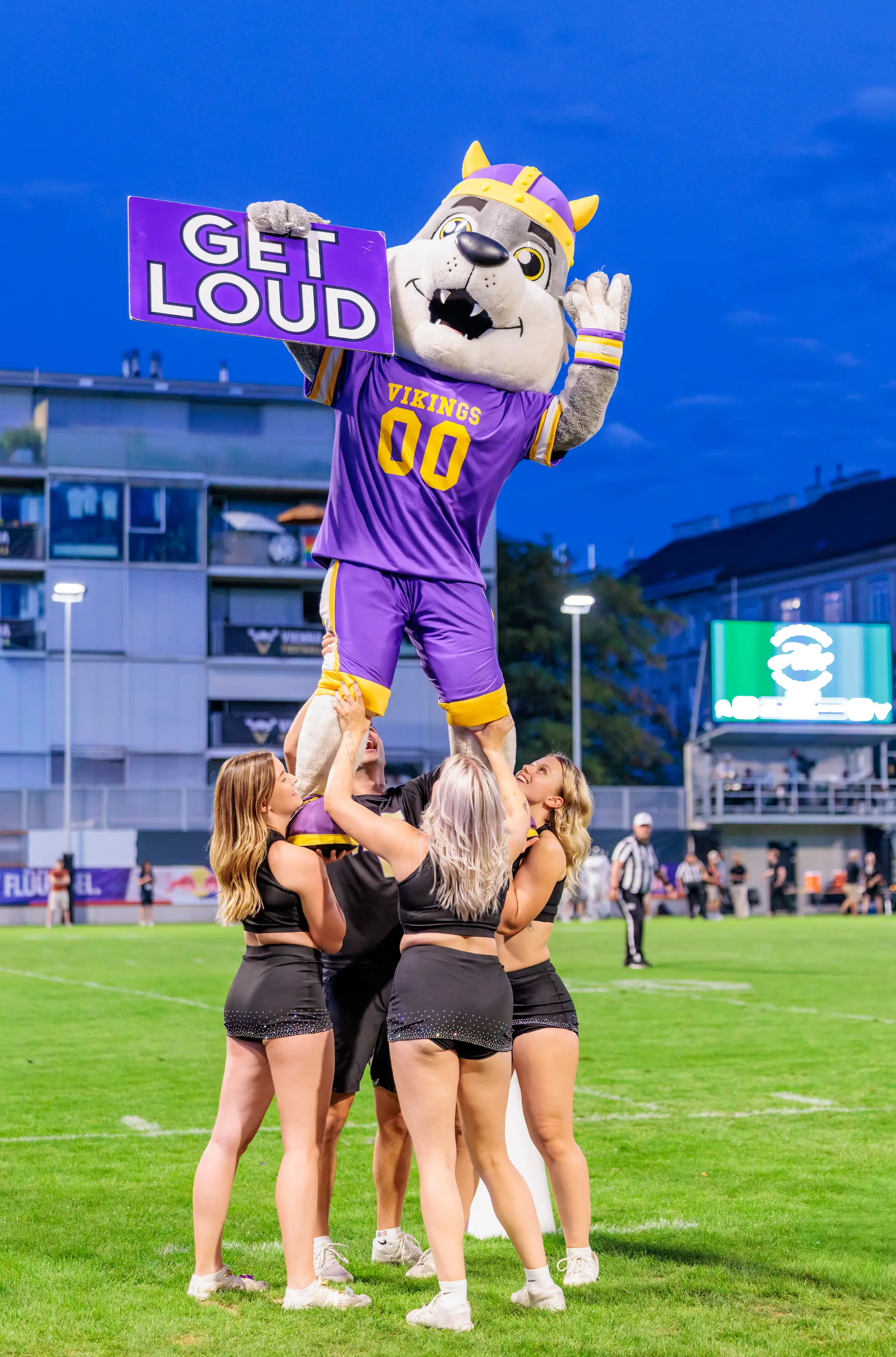 Das Vikings-Maskottchen wird über die Köpfe gehoben und zeigt der Menge das „GET LOUD“-Schild, umringt von Tänzerinnen des Cheer Squads – Stimmungsmoment bei der Pause.