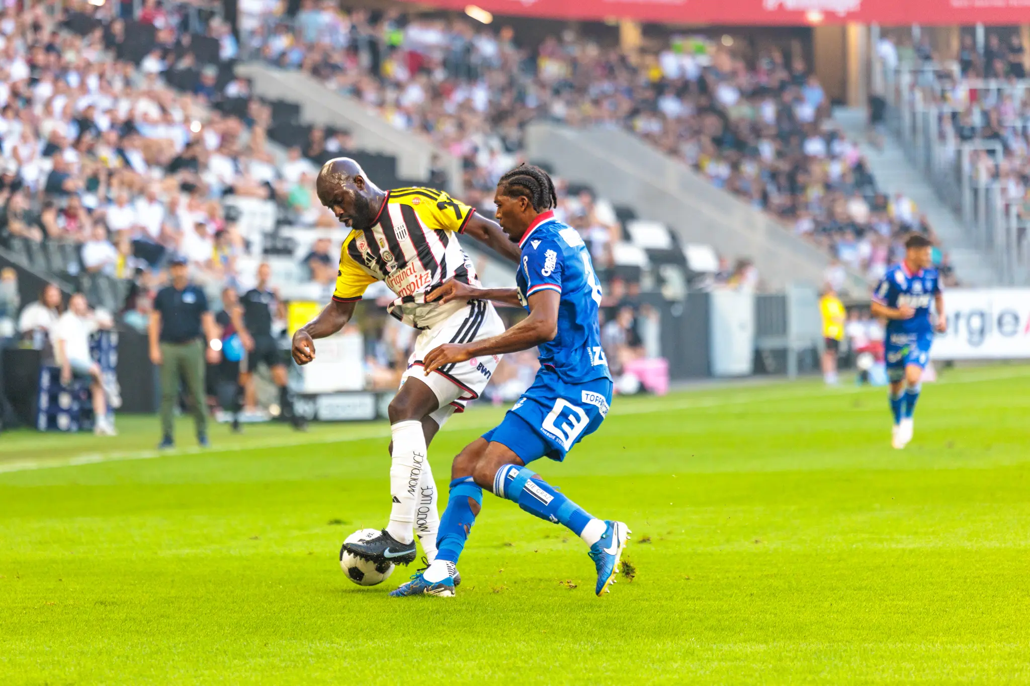 Adeniran kämpft im direkten Duell gegen einen GAK-Verteidiger um den Ball auf dem Rasen des LASK-Stadions