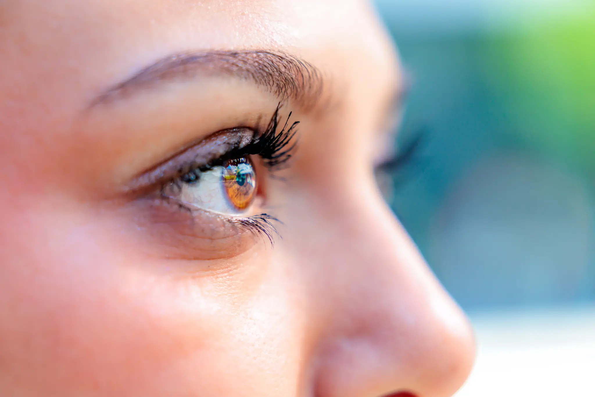 Nahaufnahme eines braunen menschlichen Auges mit langen Wimpern mit Reflexionen, wobei der Fokus auf dem Auge liegt und die Haut und die Augenbrauen deutlich sichtbar sind. 