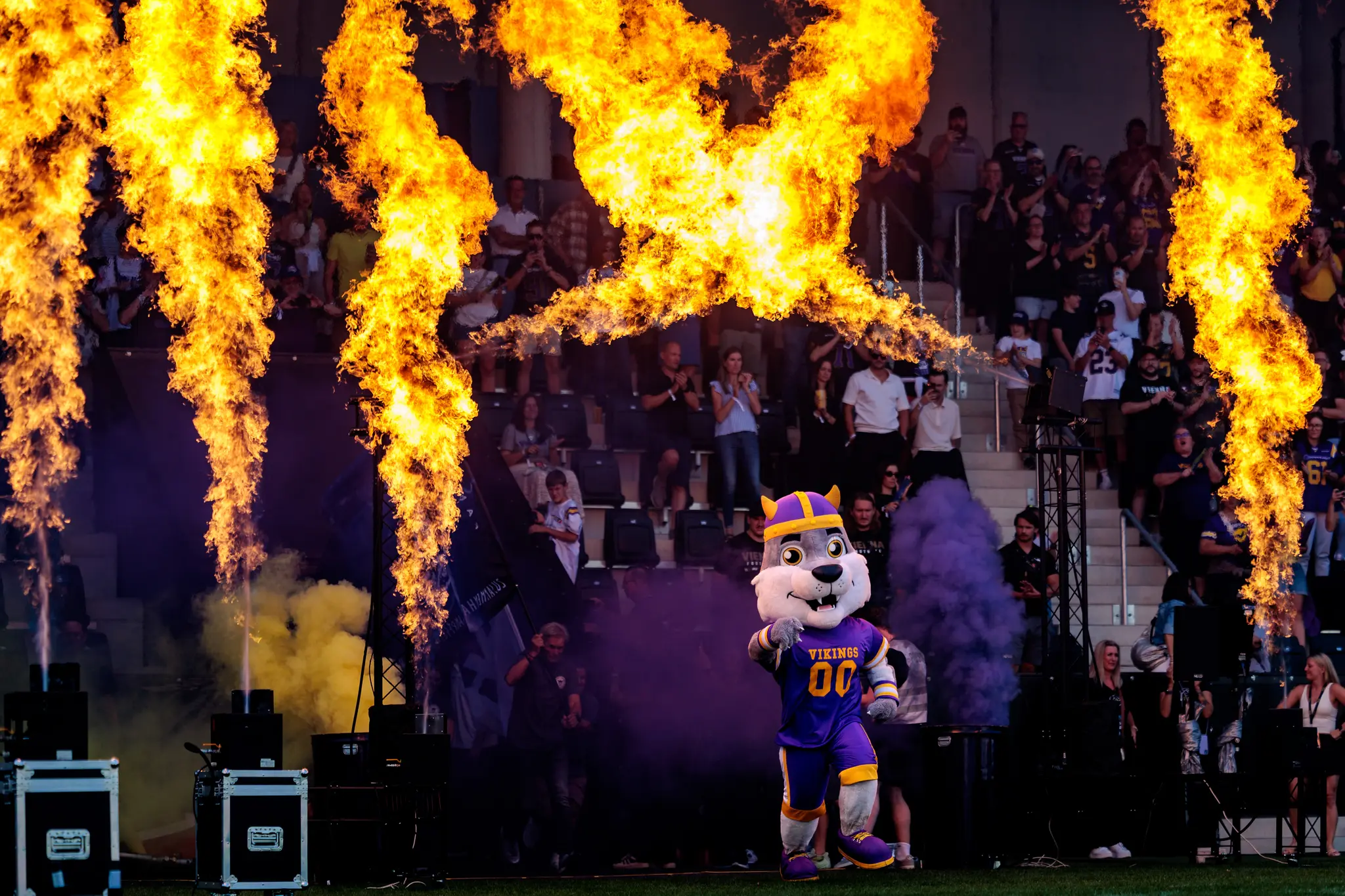 Beim Einlauf mit Feuer-Show läuft das Maskottchen der Vienna Vikings mit lila Helm und goldenen Hörnern vor der Tribüne vorbei, während rechts und links Flammen emporflackern.