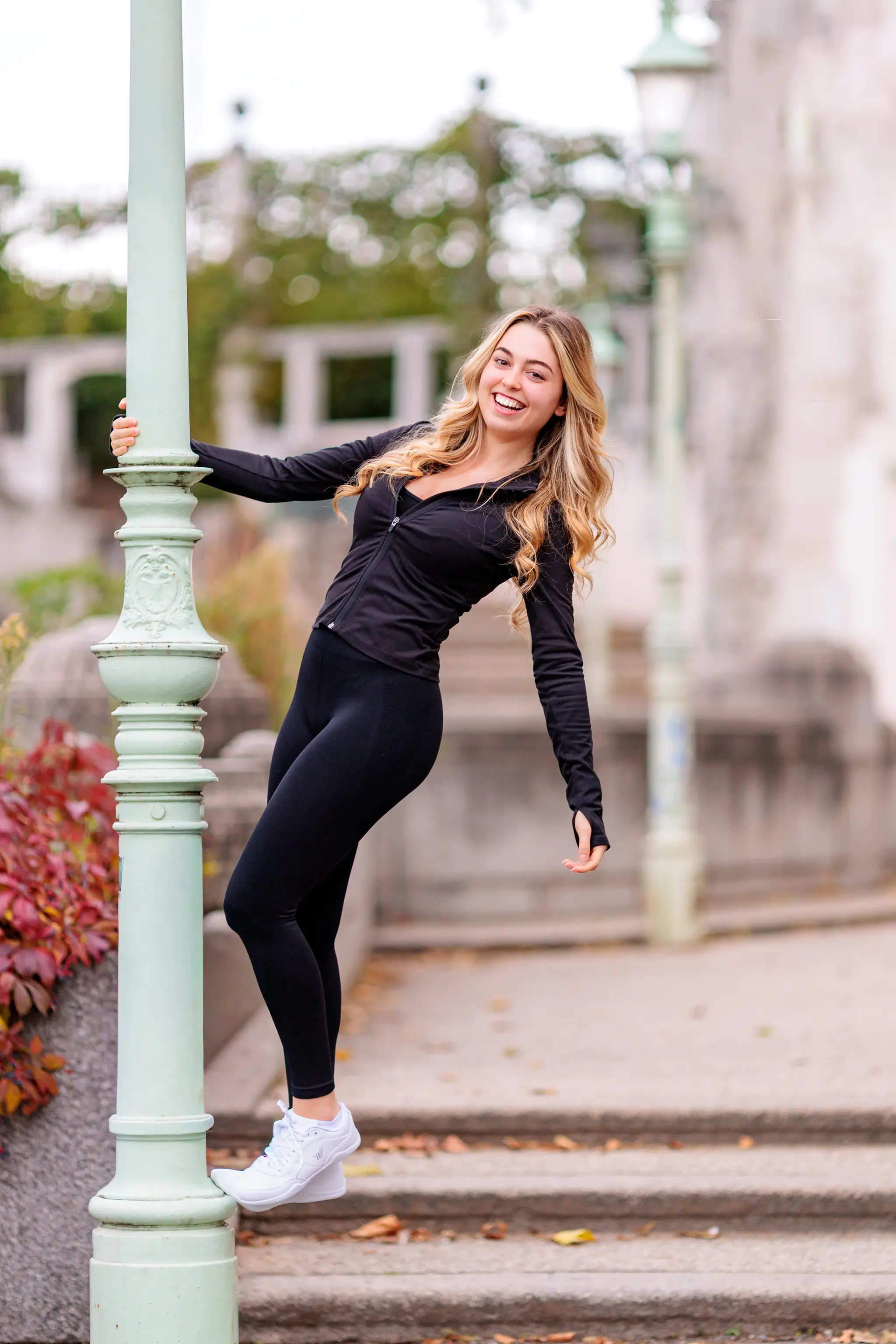 Model Valentina lehnt sich während ihres Fotoshootings im Wiener Stadtpark lachend und in schwarzer Sportkleidung an eine hellgrüne, verzierte Laterne