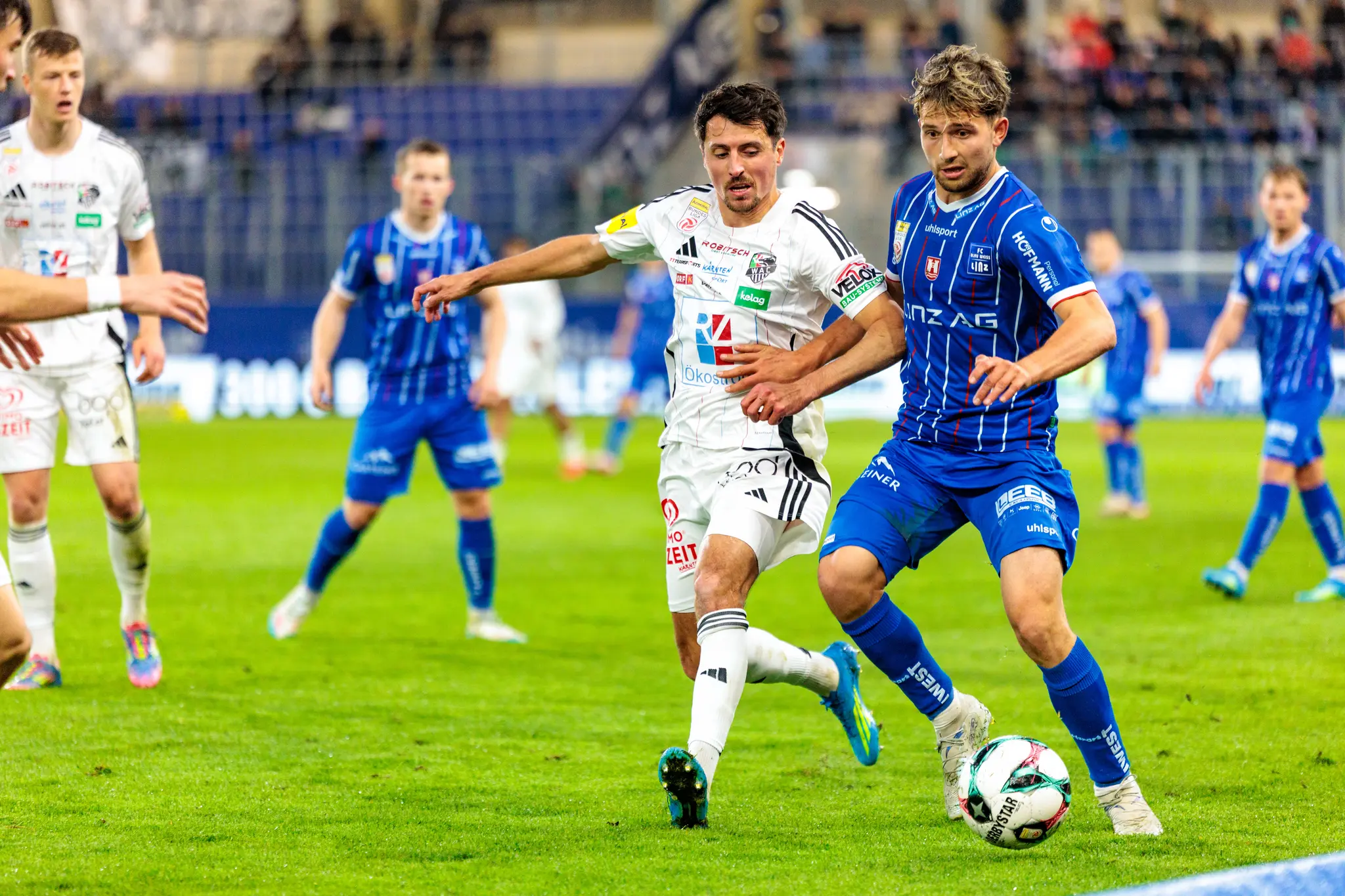 Ein Spieler des FC Blau-Weiß Linz und ein Spieler des Wolfsberger AC führen einen intensiven Zweikampf um den Ball aus