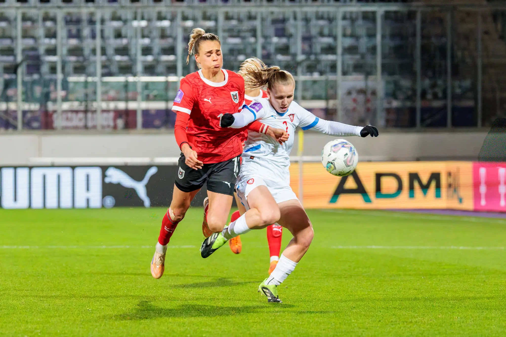 Eine österreichische Nationalspielerin im roten Trikot bestreitet einen intensiven Zweikampf gegen eine tschechische Spielerin im weißen Dress, die den Ball spielt