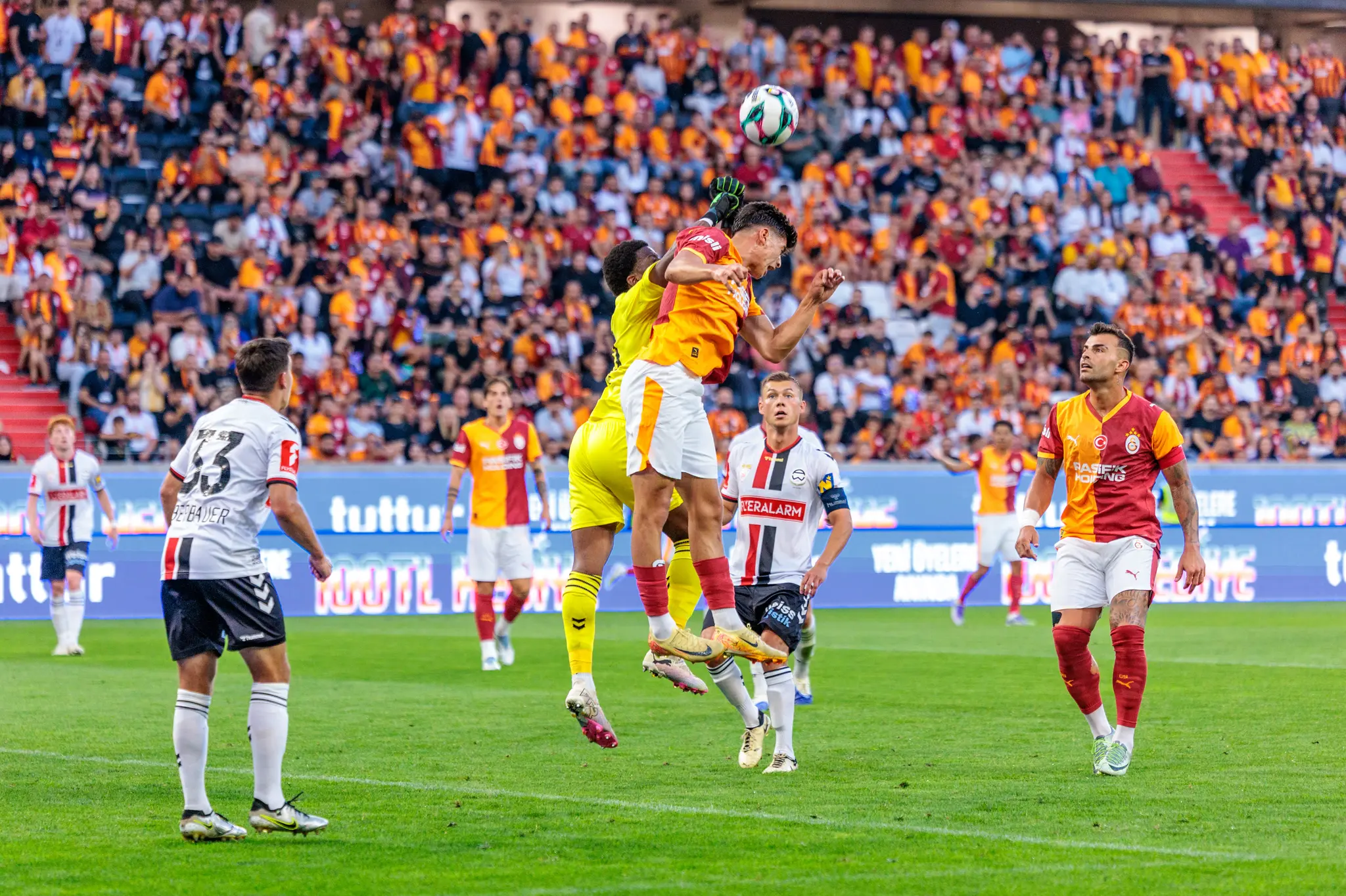 Spieler von Galatasaray und Admira Wacker duellieren sich bei einem Kopfball in der Luft während eines Fußballspiels der Nero Summer Series vor begeisterten Fans 
