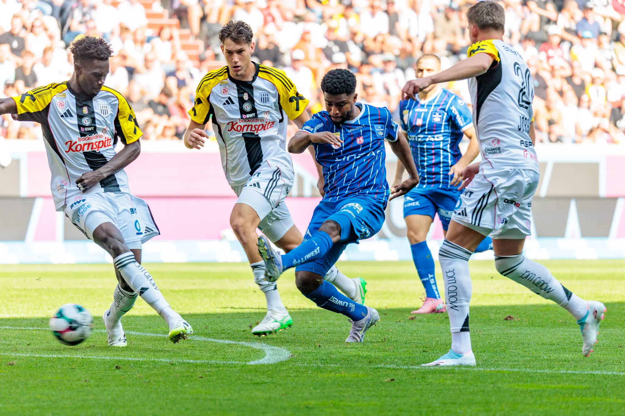 Paul Mensah vom FC Blau-Weiß Linz im Dribbling am Ball, bedrängt von mehreren LASK-Spielern während des Linzer Derbys