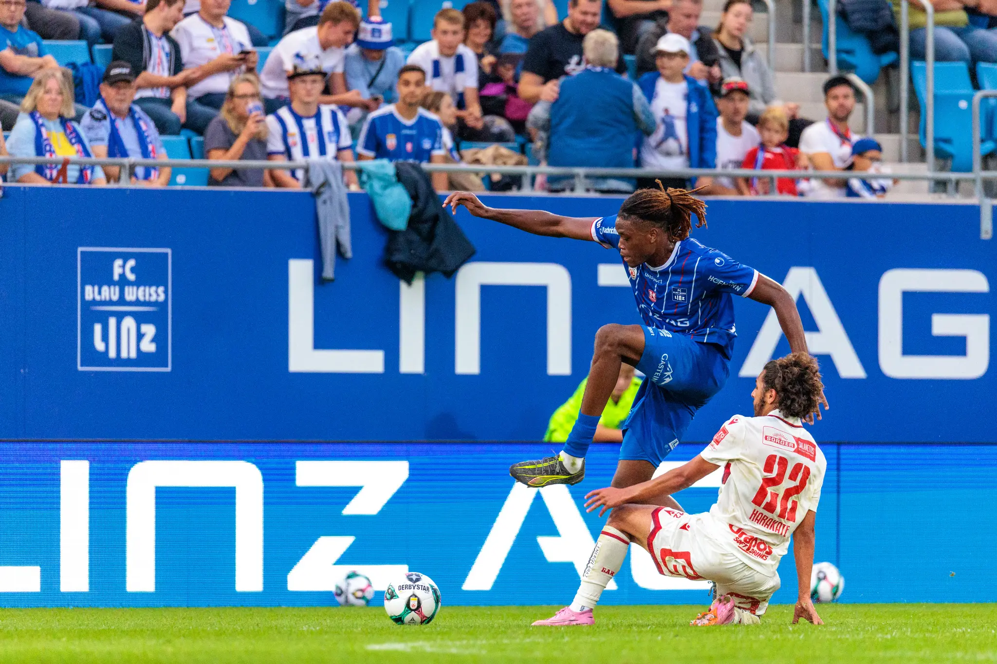 Alem Pasic vom FC Blau-Weiß Linz überspringt in einem dynamischen Zweikampf die Grätsche des am Boden liegenden GAK-Spielers Ramiz Harakate