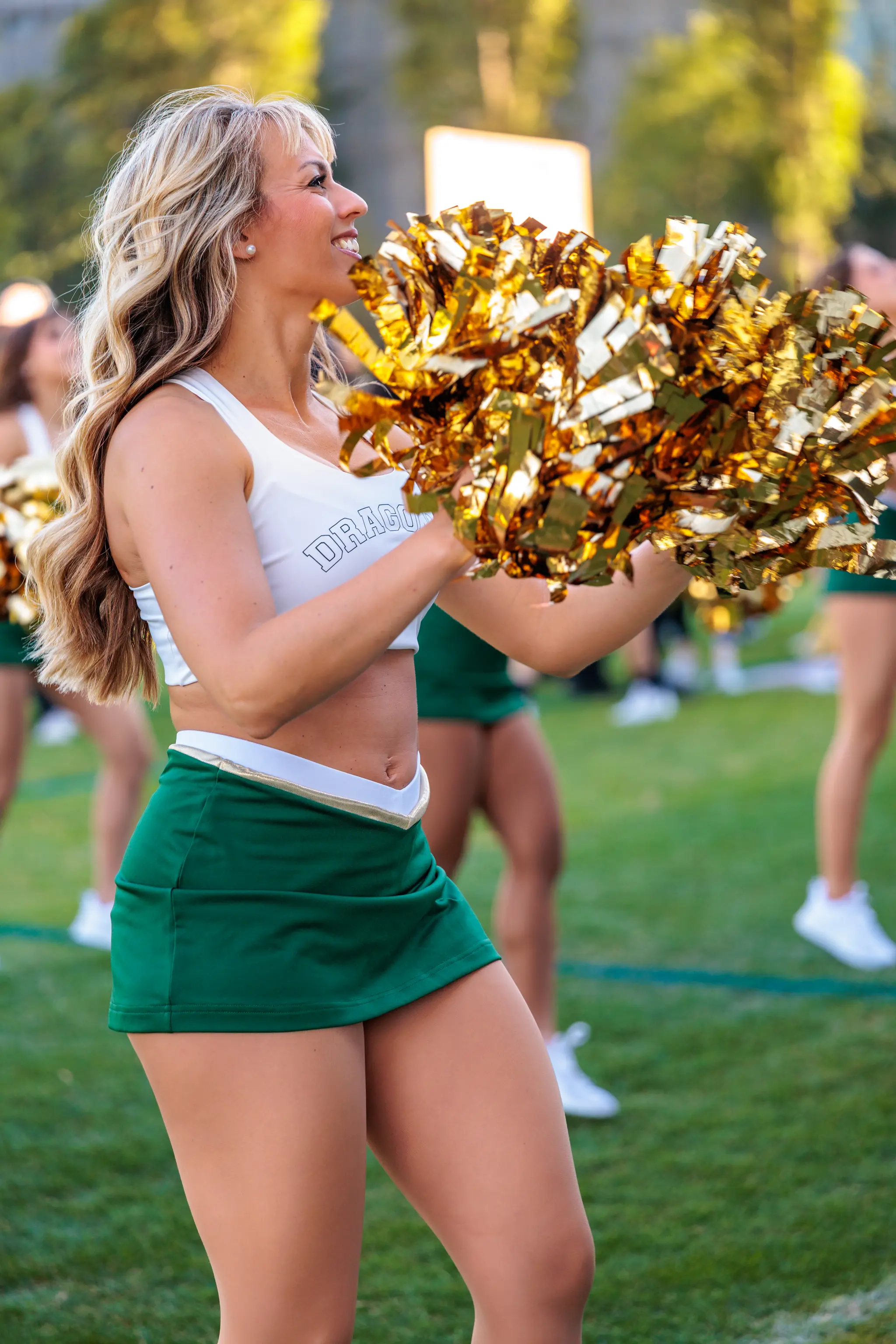 Dragons-Cheerleaderin im Seitenprofil lächelnd mit goldenen Pom-Poms bei der Halbzeitshow 2026