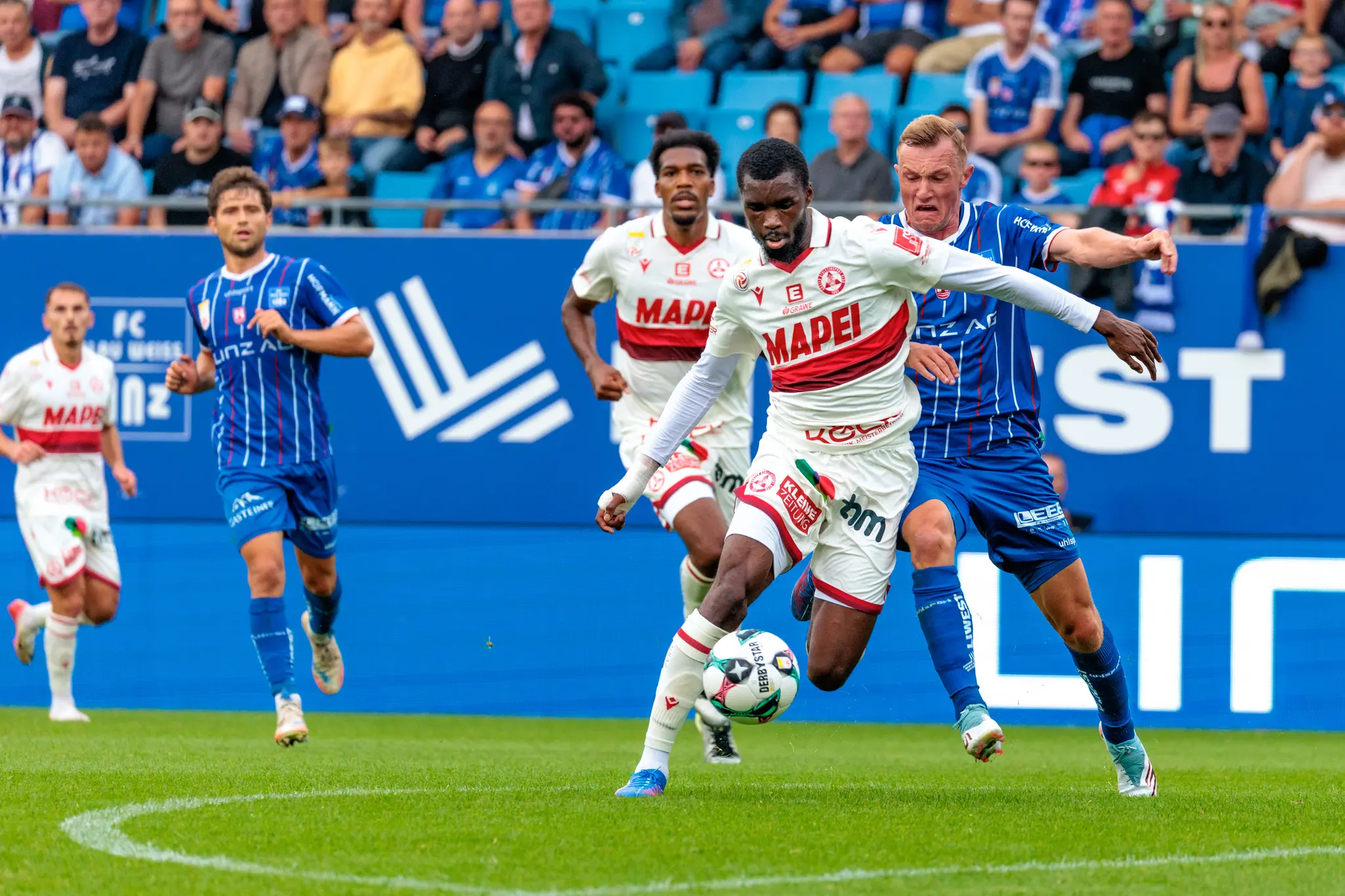 Sadik Fofana im weißen GAK-Trikot dribbelt den Fußball unter Bedrängung eines gegnerischen Spielers von Blau-Weiß Linz