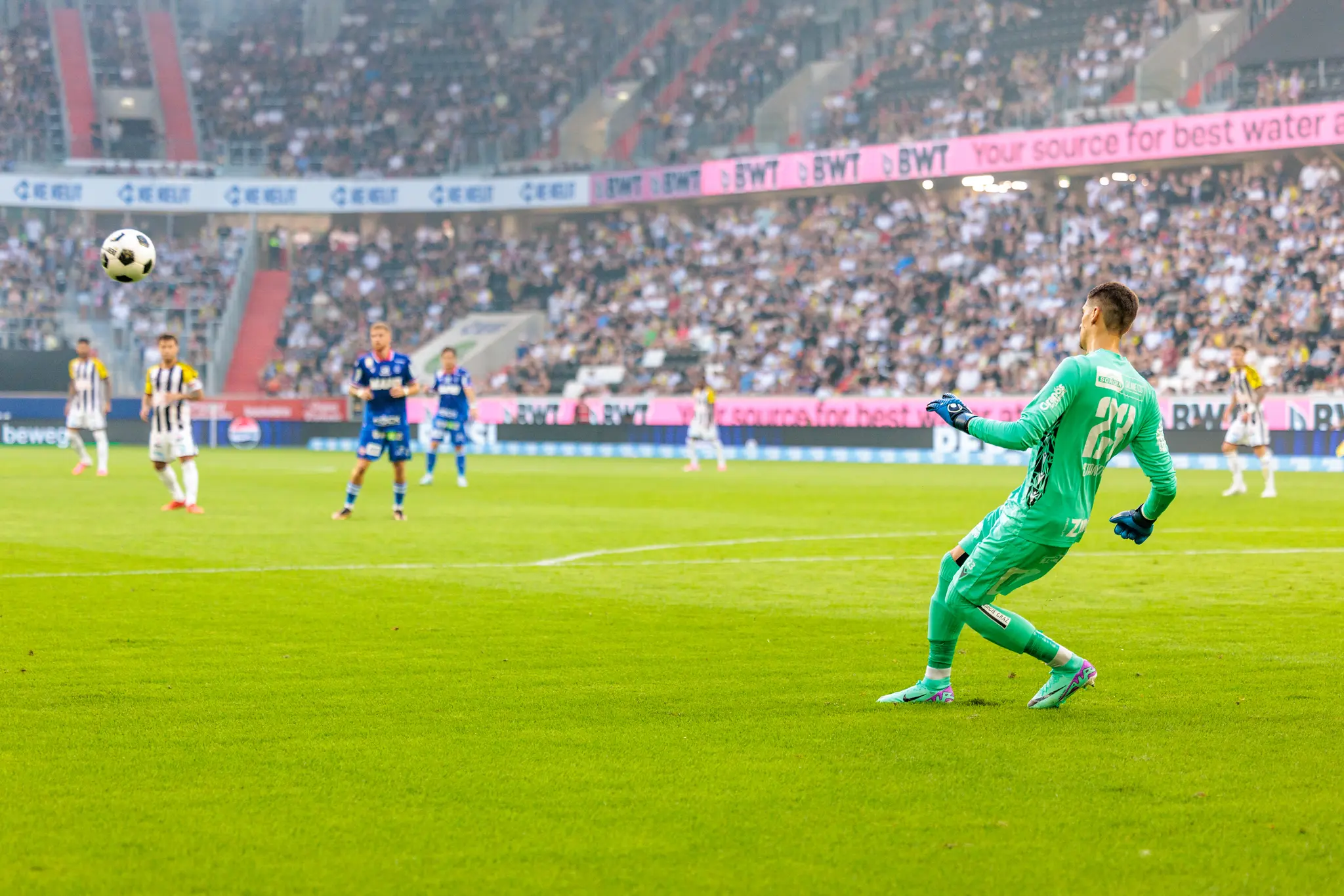 GAK-Torhüter Stankovic im grünen Trikot schlägt den Ball aus dem Strafraum heraus, während beide Teams auf dem Platz positioniert sind