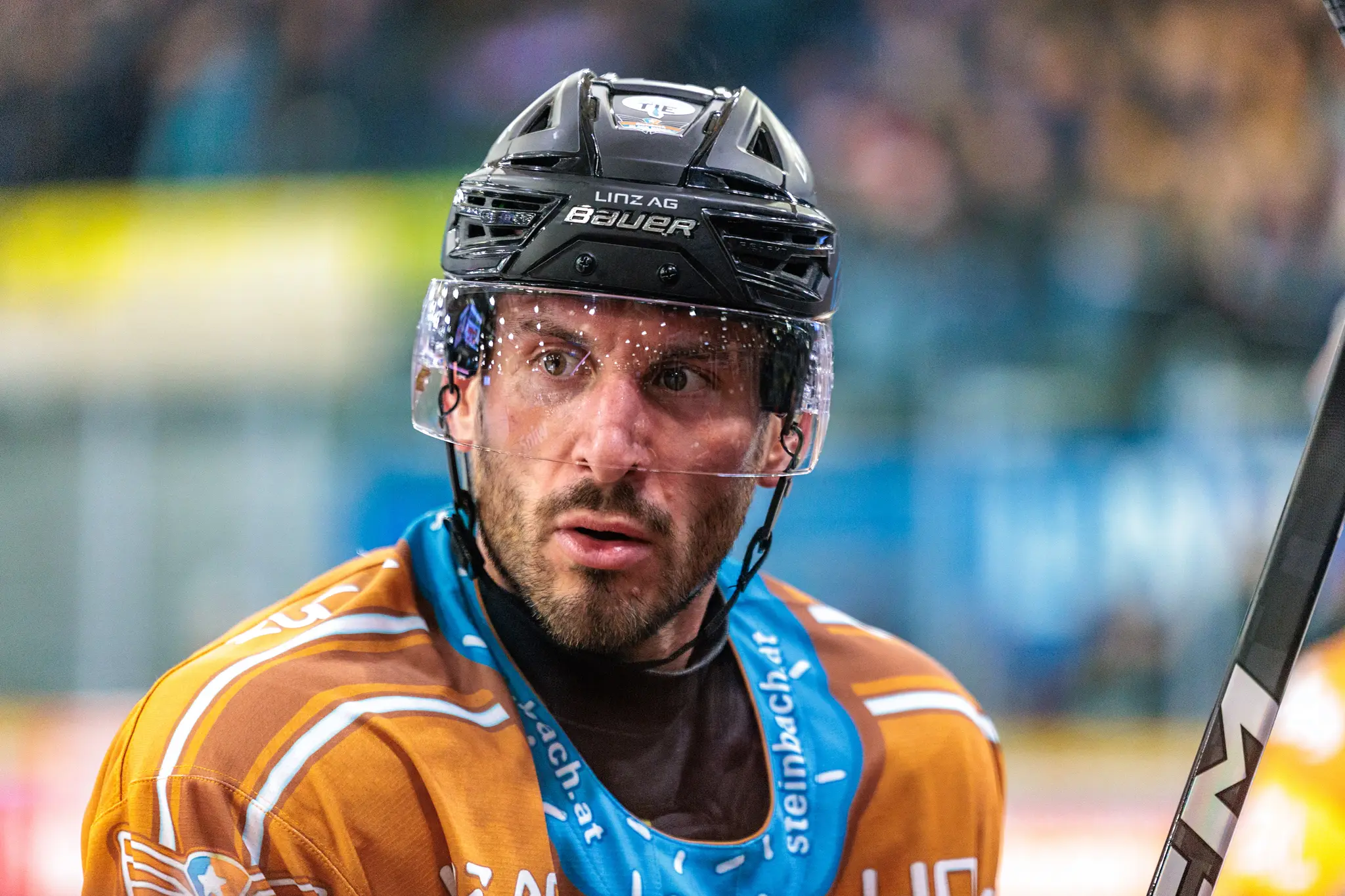 Graham Knott, Eishockeyspieler der Black Wings Linz, blickt in seinem orangefarbenen Trikot und Helm mit Visier fokussiert während eines Spiels
