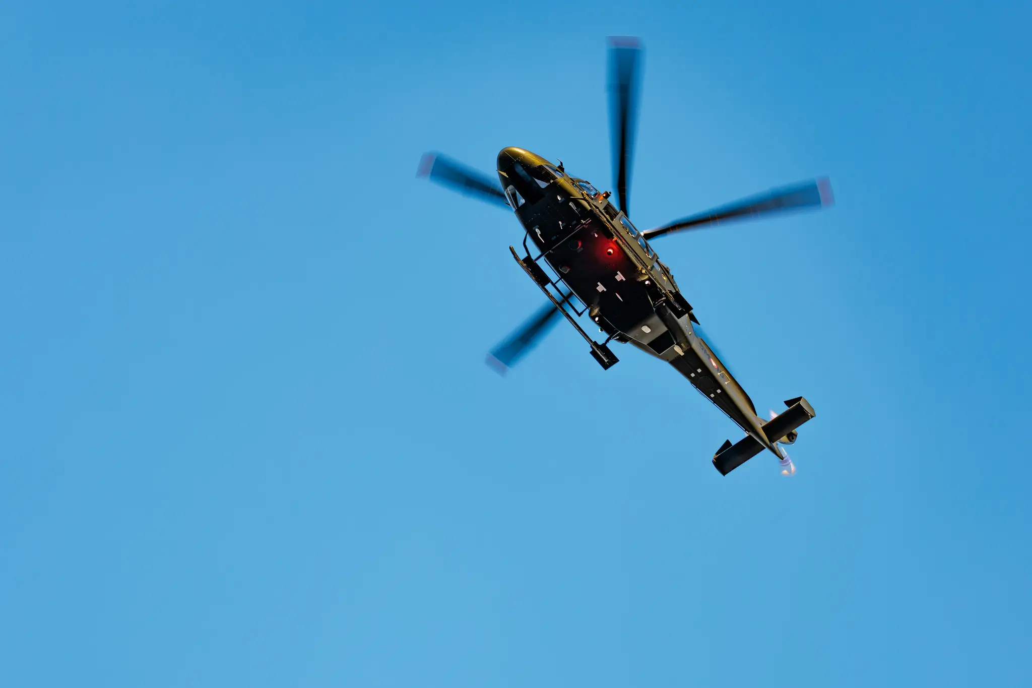 Ein Militärhubschrauber vom Typ Leonardo AW169M „Lion“ mit laufendem Rotor fliegt durch den Himmel, der sich in hellem Blau mit Wolken zeigt.
