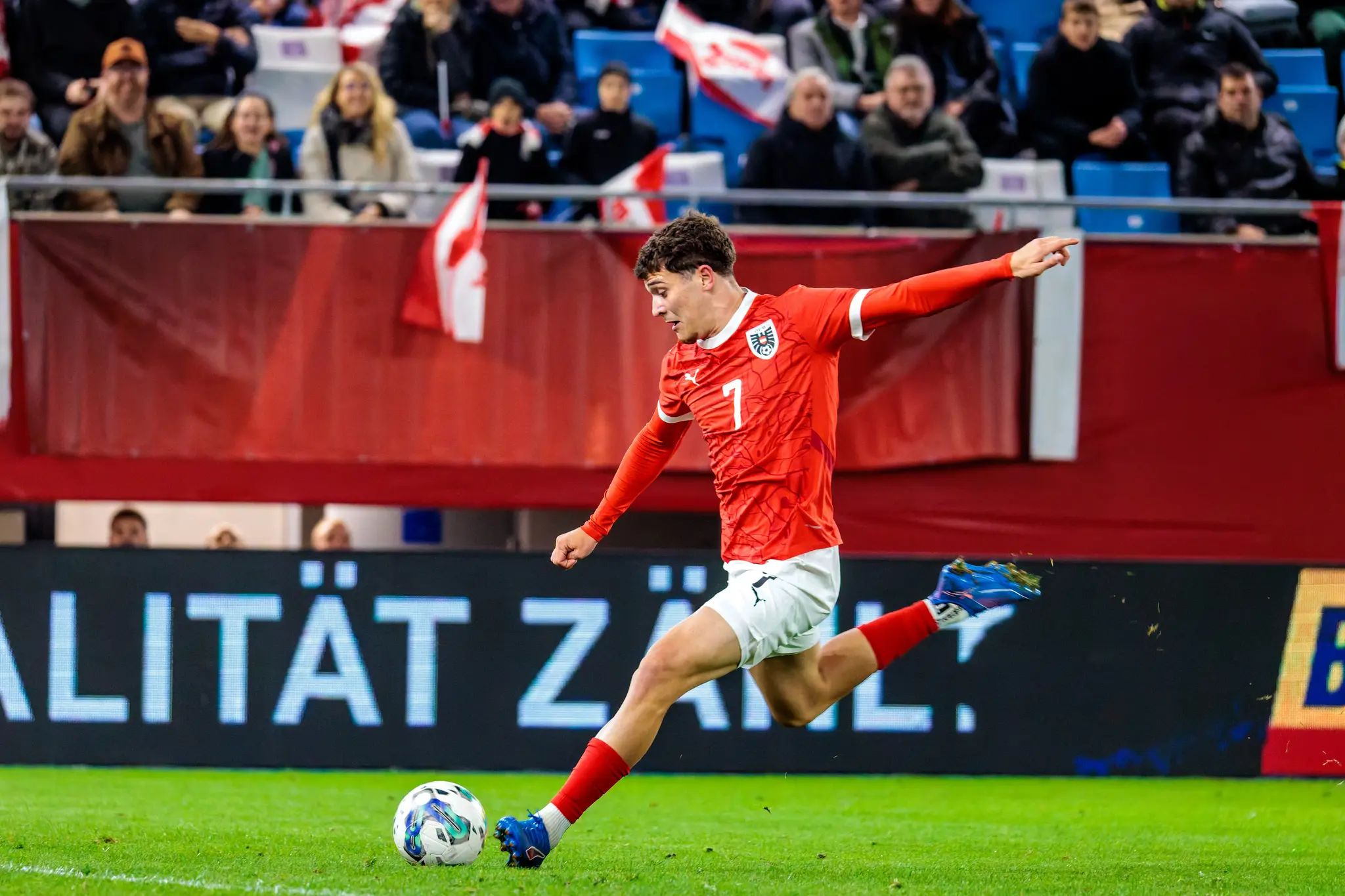 Der österreichische U21-Nationalspieler Moritz Wels schlägt in seinem roten Trikot mit der Nummer 7 eine Flanke mit dem rechten Fuß