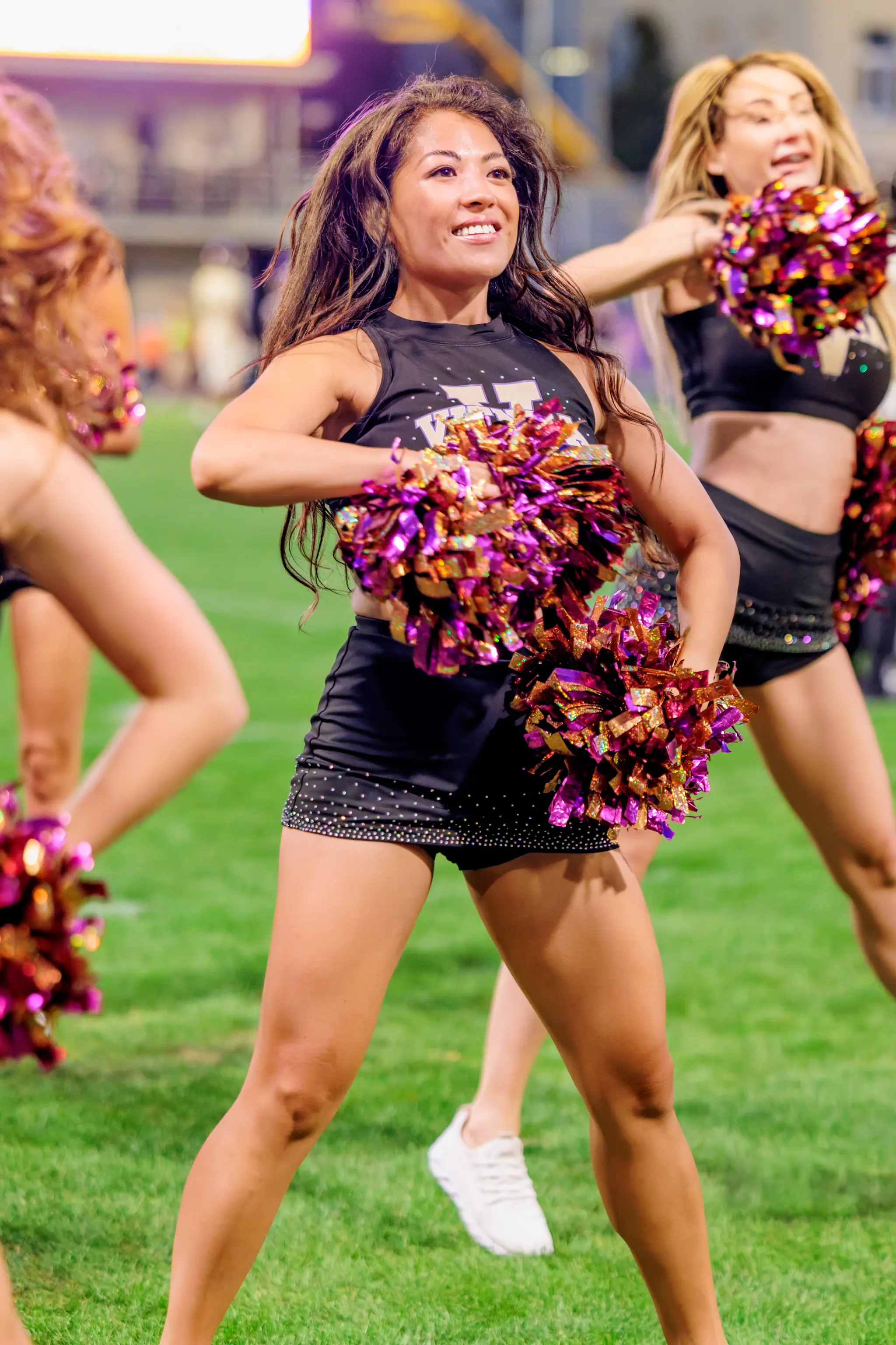 Lächelnd hält eine Tänzerin des Vienna Vikings Cheer Squads die lila-goldenen Pompons vor der Brust, hinter ihr leuchten die Tribünen des Stadions im Abendlicht.