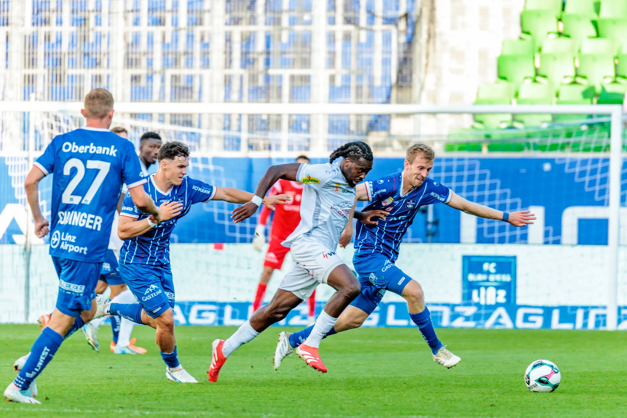 Drei Fußballspieler im intensiven Laufduell um den Ball während eines Bundesligaspiels zwischen Blau-Weiß Linz und Altach
