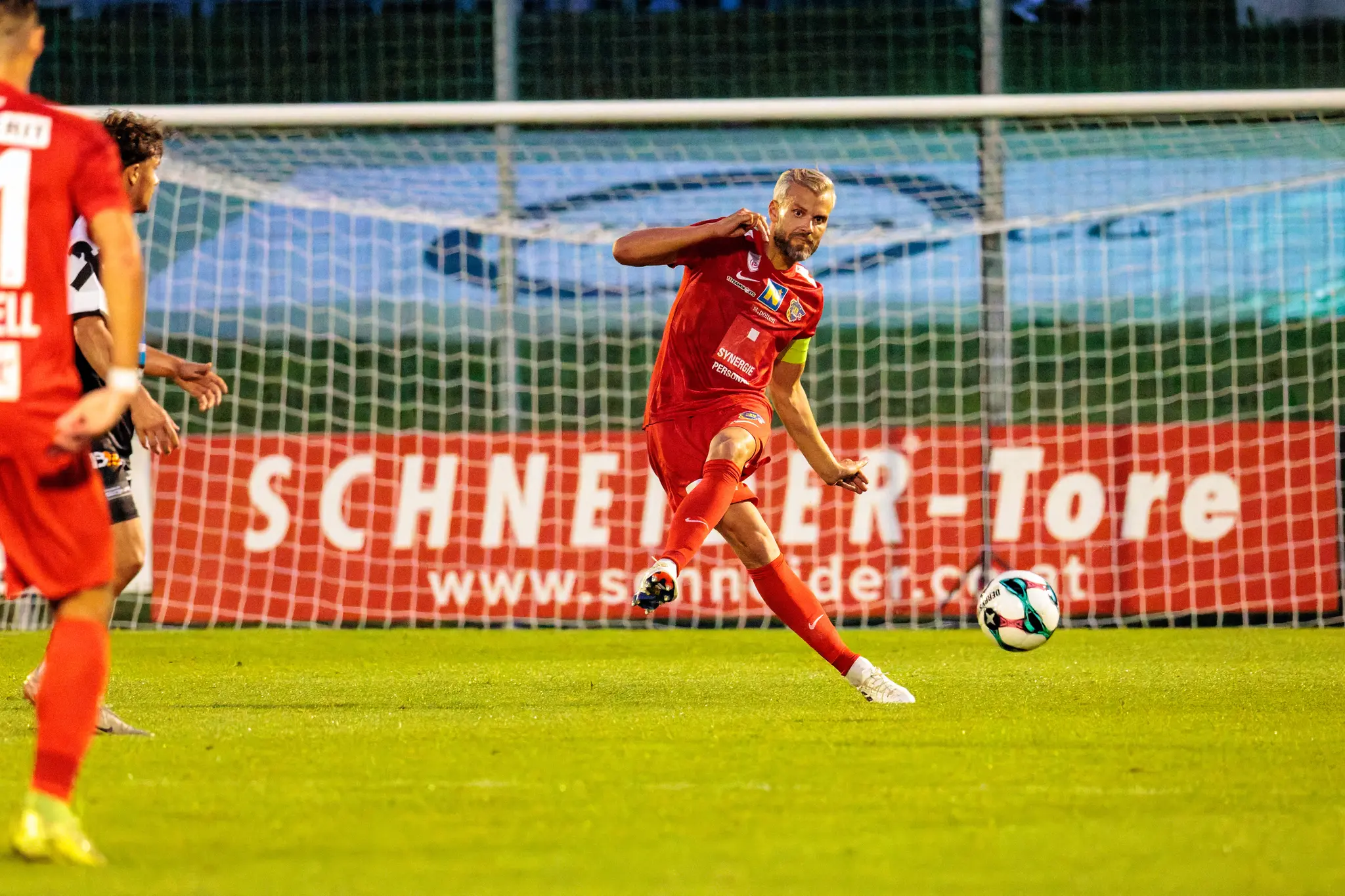Ein Spieler des SKN St. Pölten im roten Trikot mit Kapitänsbinde spielt während eines ÖFB-Cup-Spiels einen präzisen Pass nach vorne