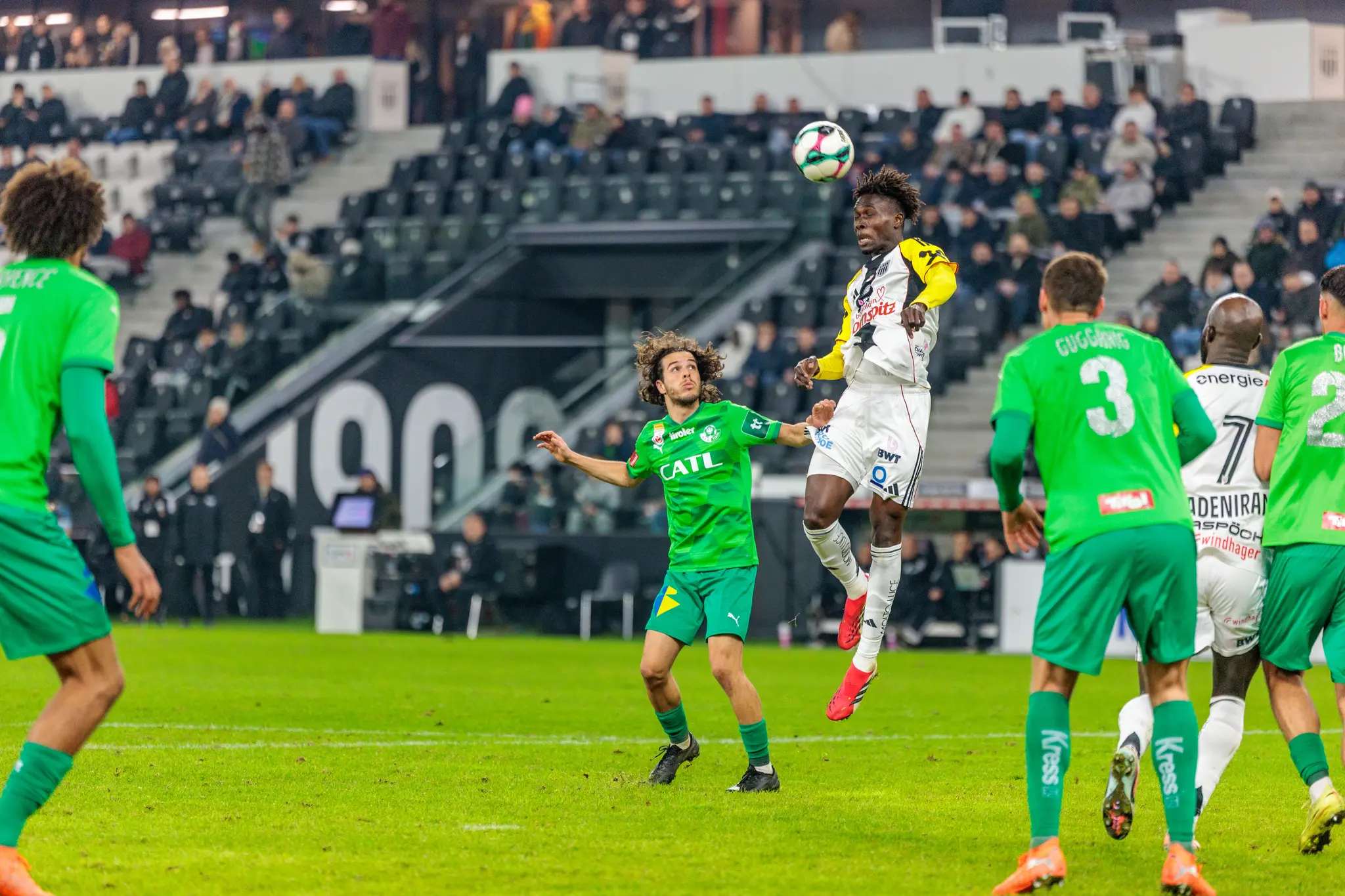 LASK-Spieler Oumar Adeniran in weiß-gelbem Trikot und ein WSG-Tirol-Spieler in Grün liefern sich ein intensives Kopfballduell um den Fußball