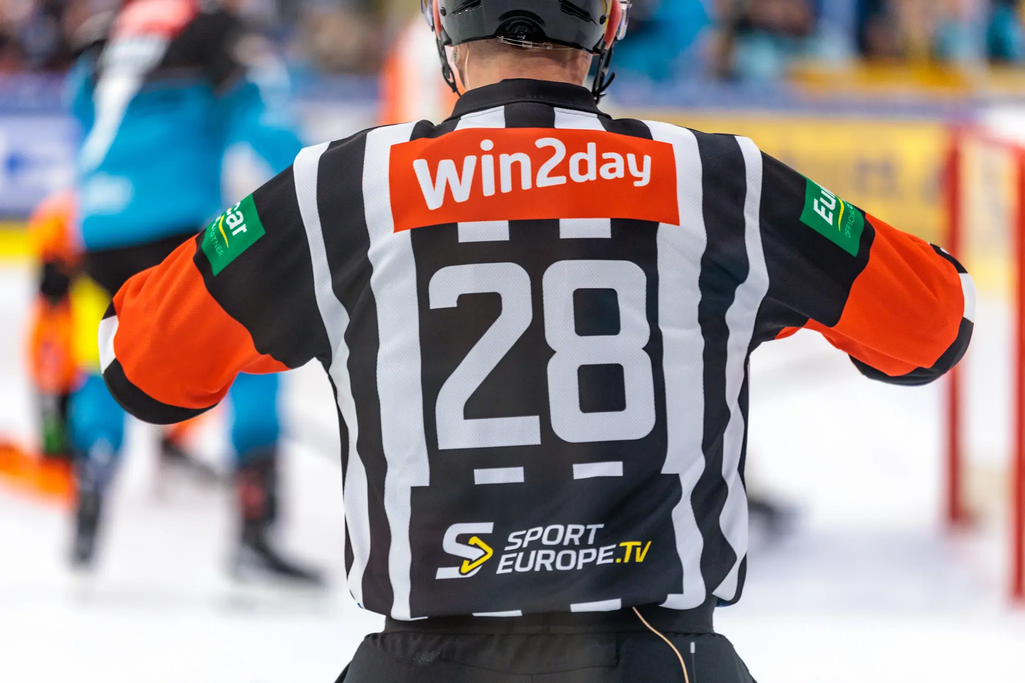 Rückansicht eines Eishockey-Schiedsrichters im schwarz-weiß gestreiften Trikot mit der Nummer 28 und dem Sponsorenlogo von Win2day auf dem Rücken