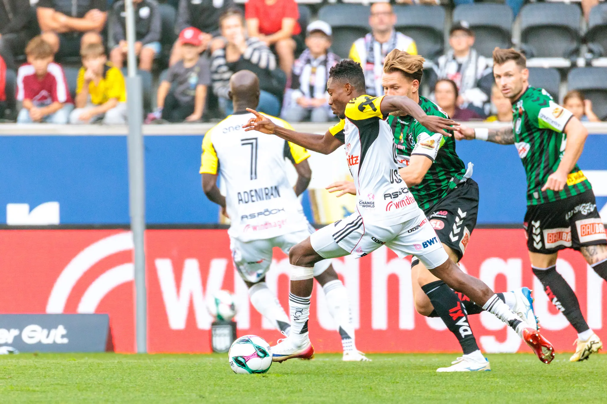 Ein LASK-Spieler in Weiß-Gelb dribbelt den Ball geschickt an einem Verteidiger des SV Ried in einem intensiven Bundesliga-Duell vorbei