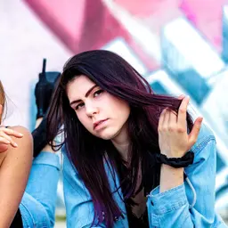 Eine junge Frau mit dunklem Haar und lila Strähnen trägt eine Jeansjacke und blickt vor einer farbigen Graffiti-Wand in die Kamera lens: 56mm F1.4 DC DN | Contemporary 018