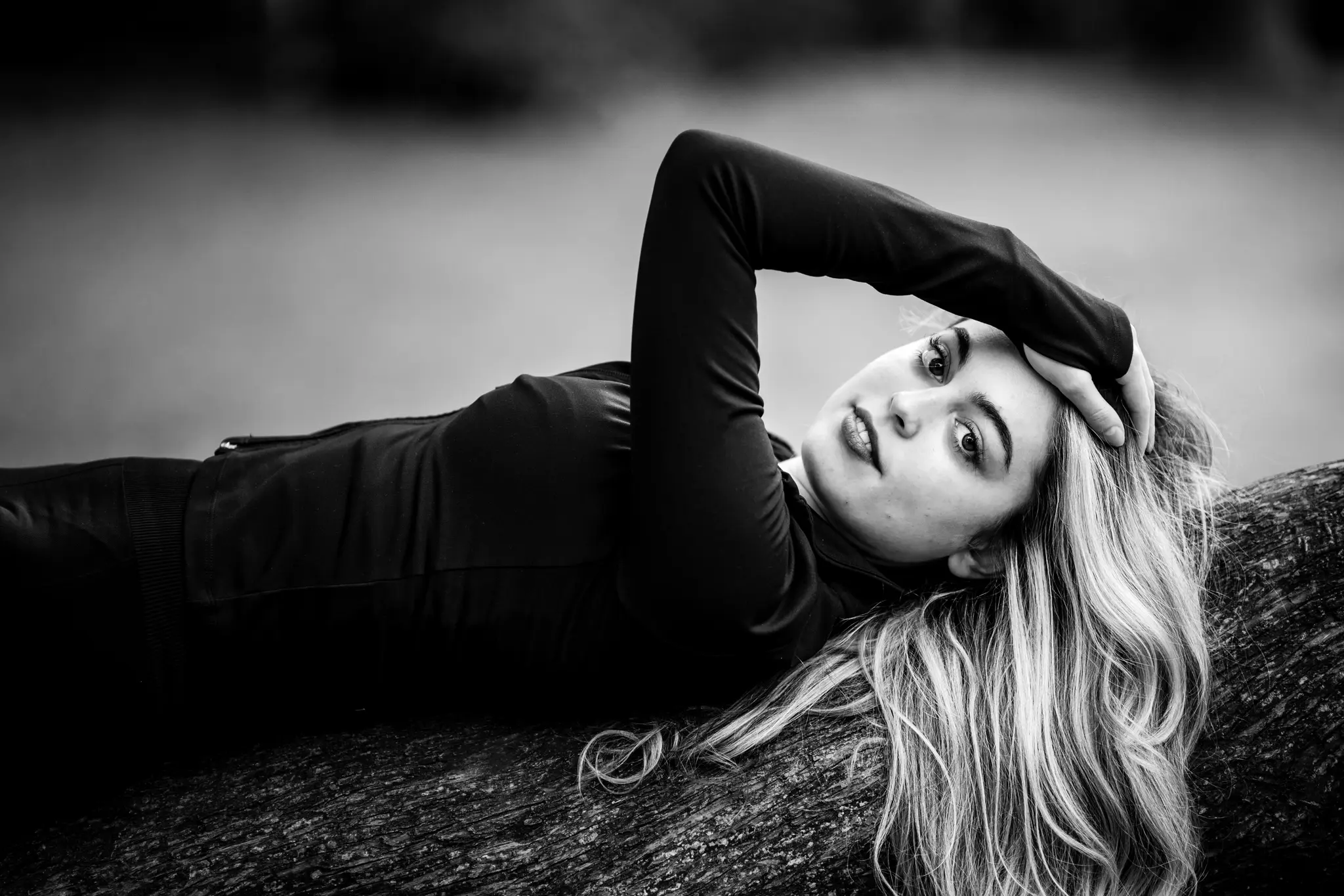 Ausdrucksstarkes Schwarz-Weiß-Porträt von Model Valentina, die auf einem Baumstamm liegt und mit der Hand im Haar direkt in die Kamera blickt