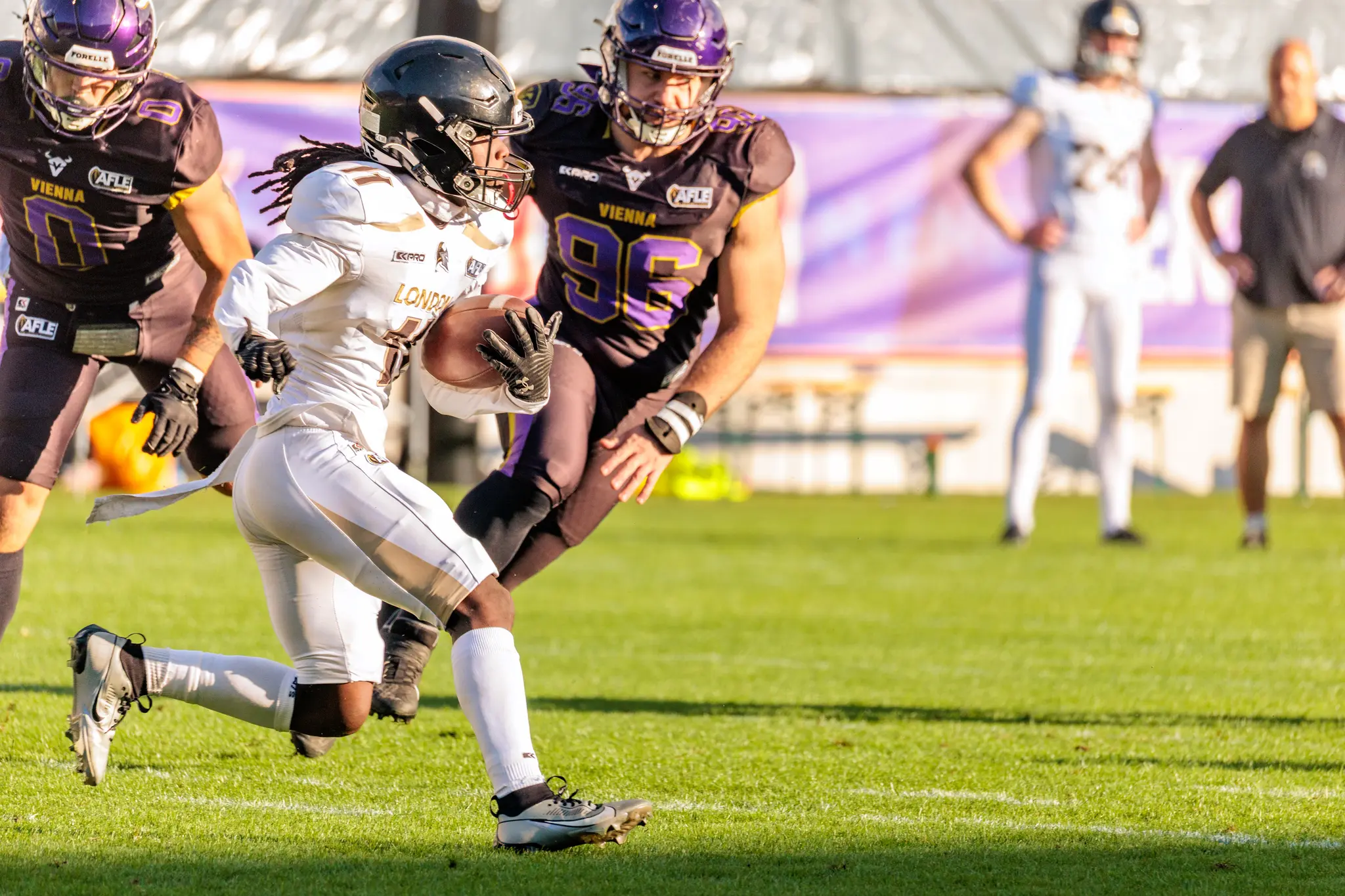 London-Spieler Nr. 11 sprintet mit dem Ball über den Rasen, verfolgt von Noel Swancar (0) und Marvin Wappl (96) der Vienna Vikings.