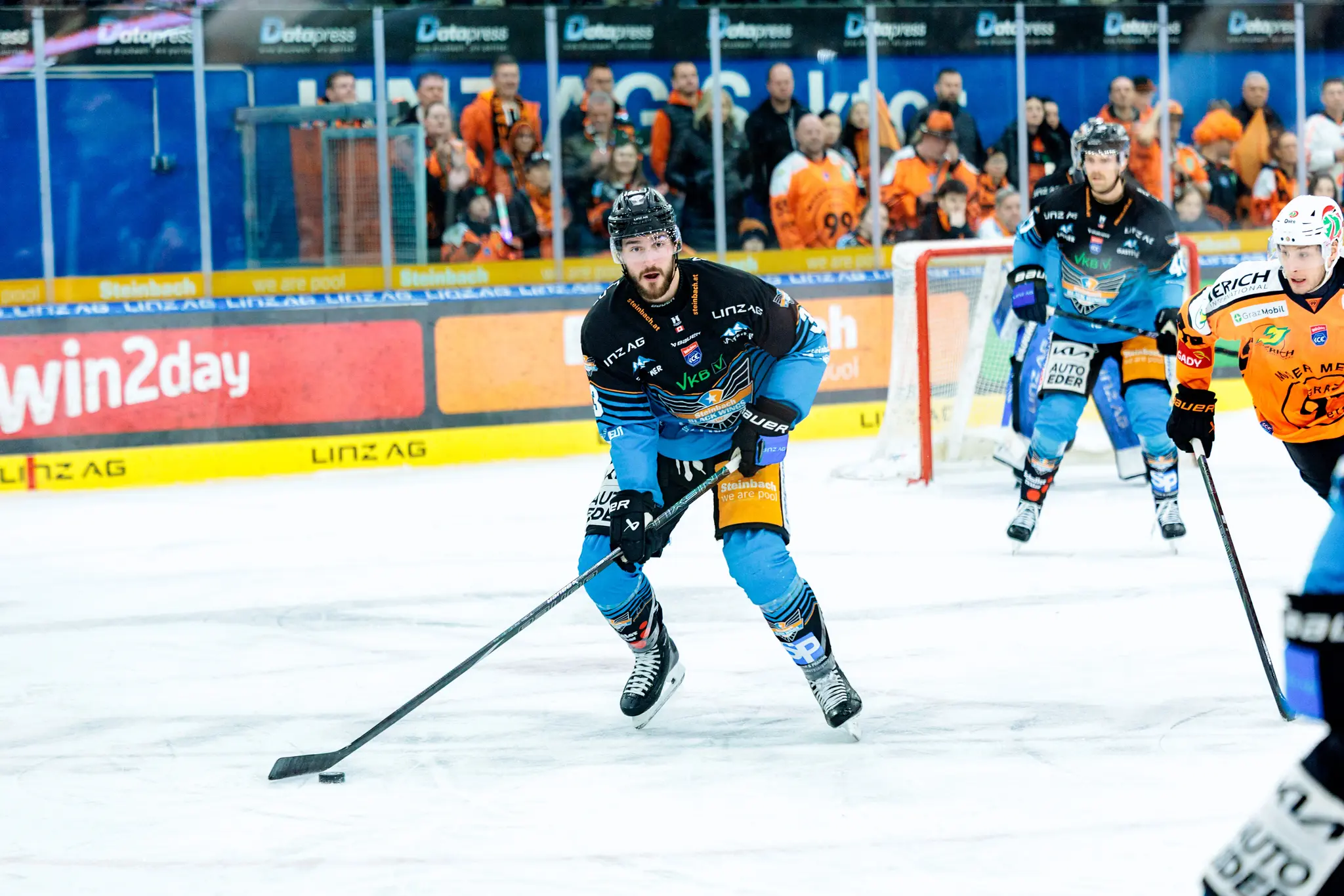 Ein Eishockeyspieler der Black Wings Linz mit schwarzem Helm und Bart führt den Puck über das Eis