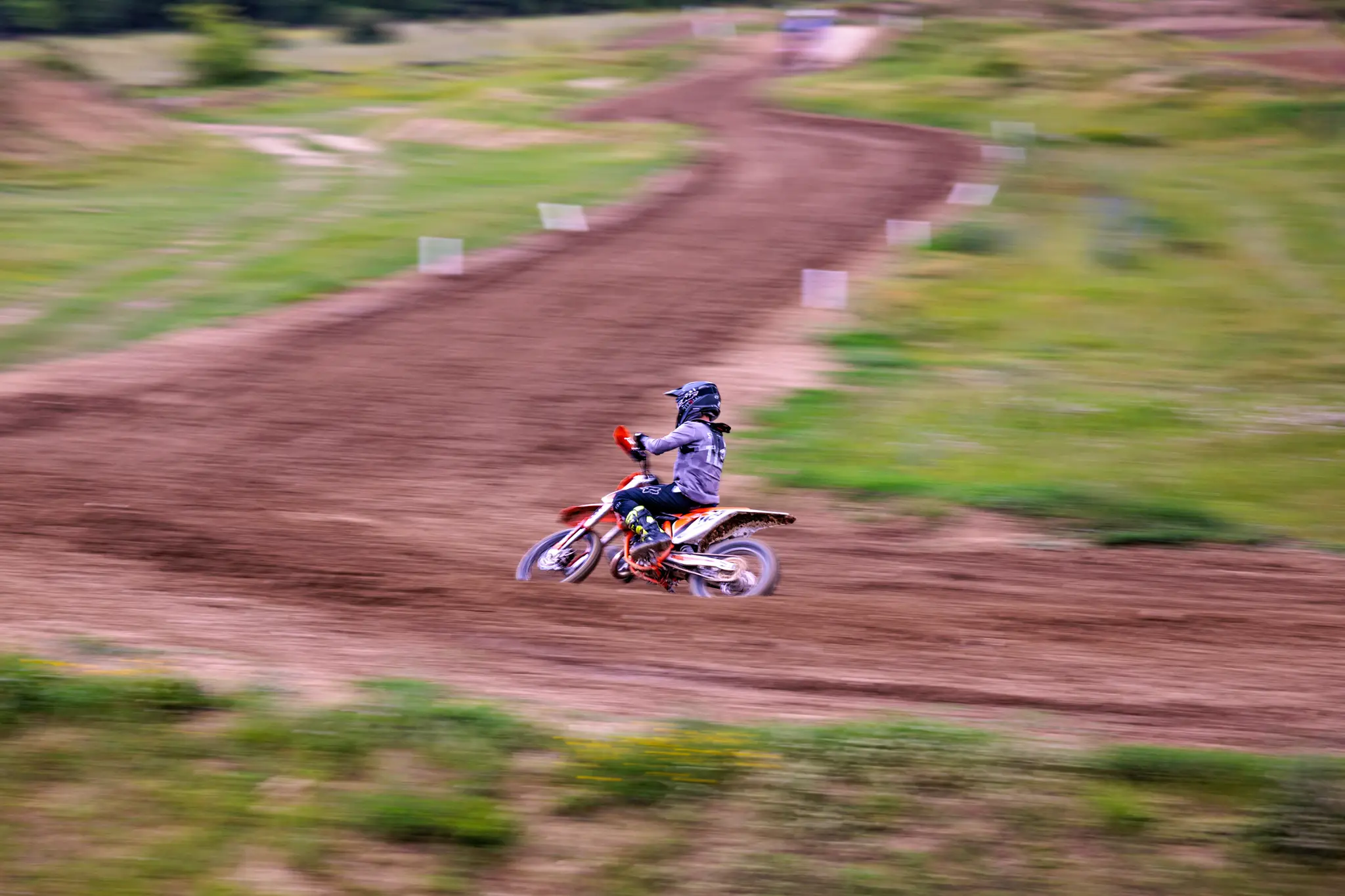 Motocross-Fahrer auf orangefarbenem Dirtbike in schneller Fahrt auf sandiger Rennstrecke 