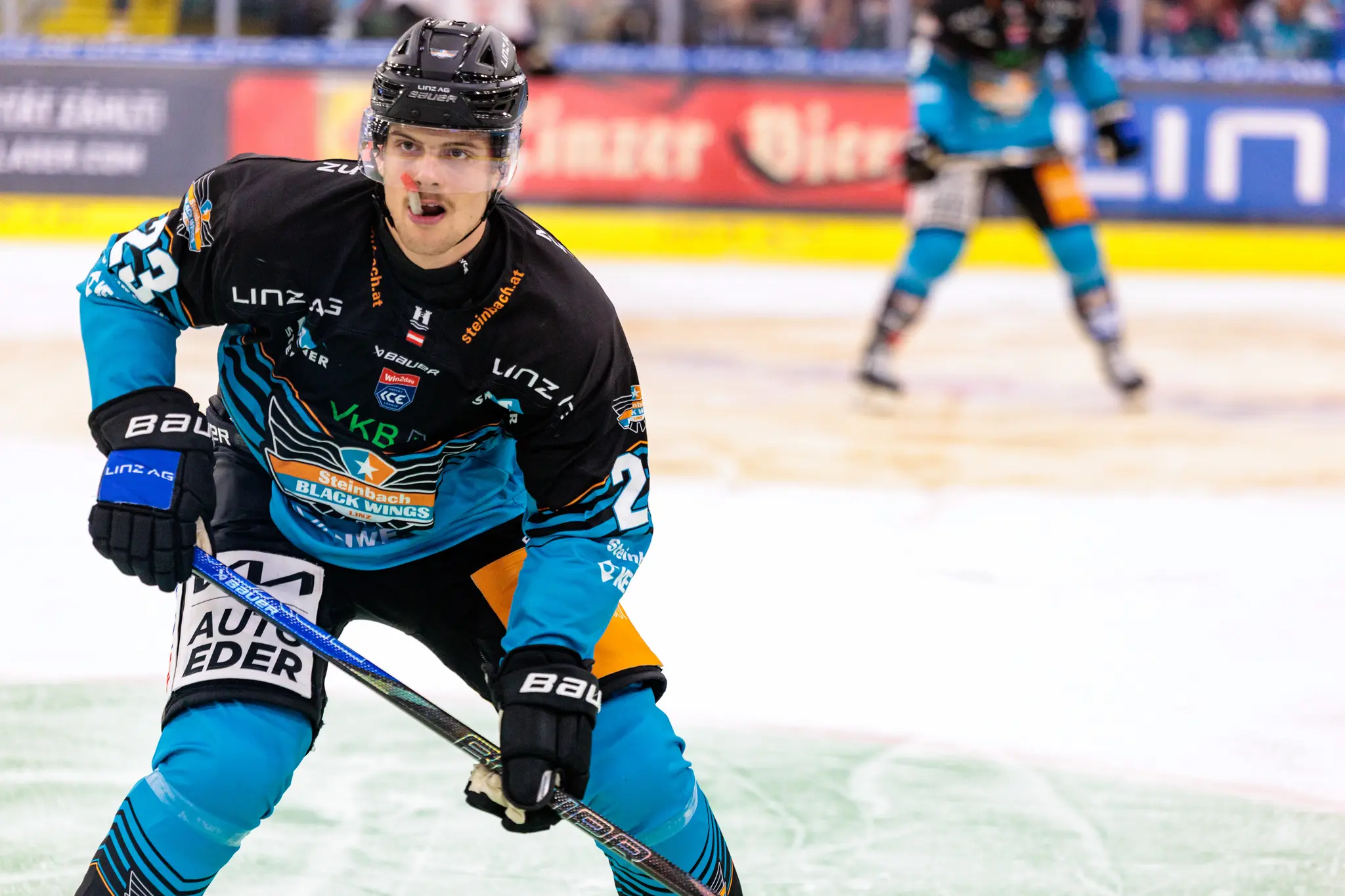 Eishockeyspieler Travis Barron der Steinbach Black Wings Linz mit der Nummer 25 in seinem schwarz-türkisen Trikot kaut auf seinem Mundschutz