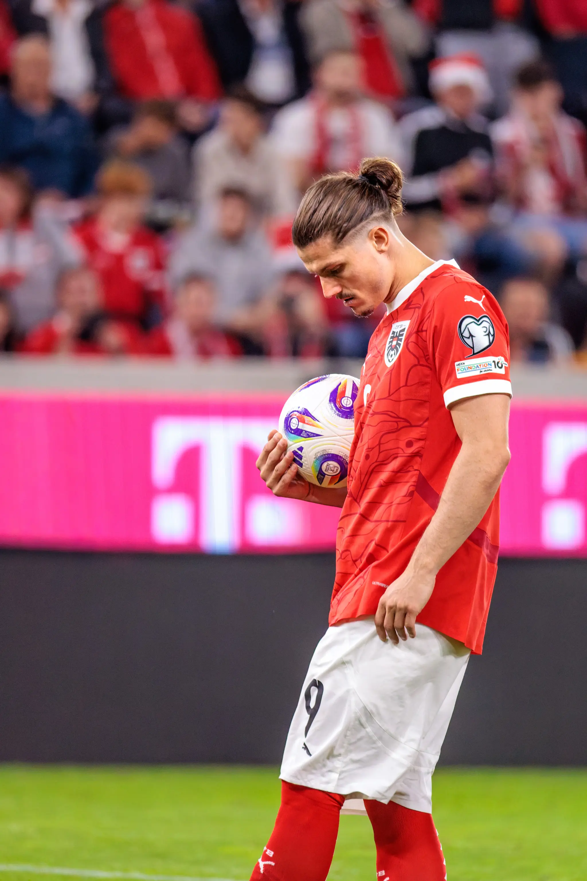 Fußballspieler Marcel Sabitzer in seinem roten Trikot mit der Nummer 9 hält nachdenklich den Fußball, bevor er zum Elfmeter antritt