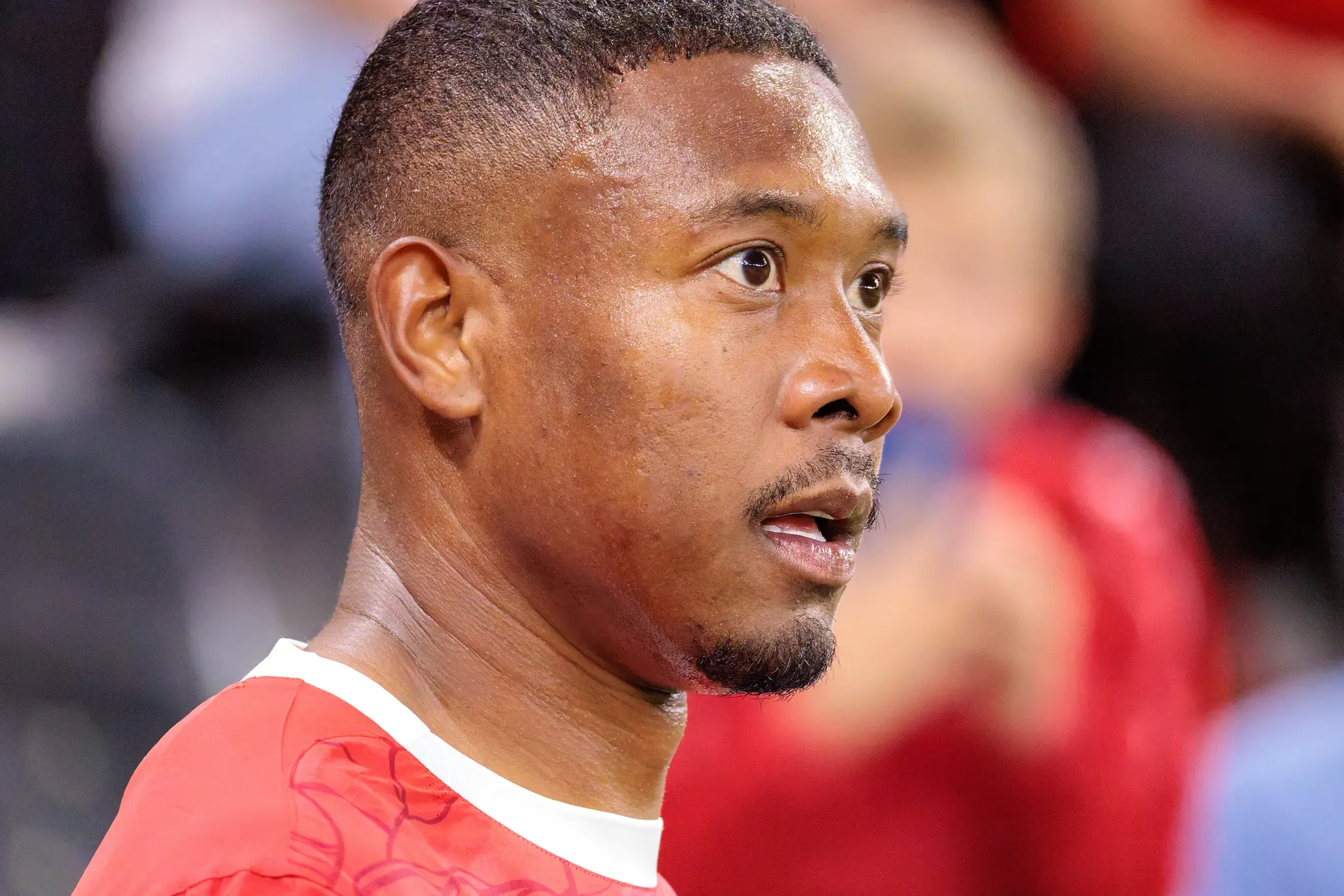 Ein Nahaufnahme-Porträt des verschwitzten Fußballspielers David Alaba, der während eines Matches nachdenklich zur Seite schaut und ein rotes Trikot trägt