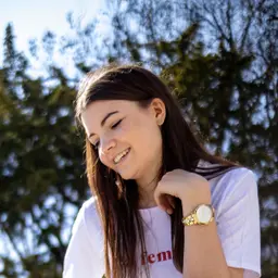 Lächelnde junge Frau mit langen Haaren und goldener Uhr in weißem T-Shirt vor unscharfem Naturhintergrund lens: Viltrox AF 23/1.4M