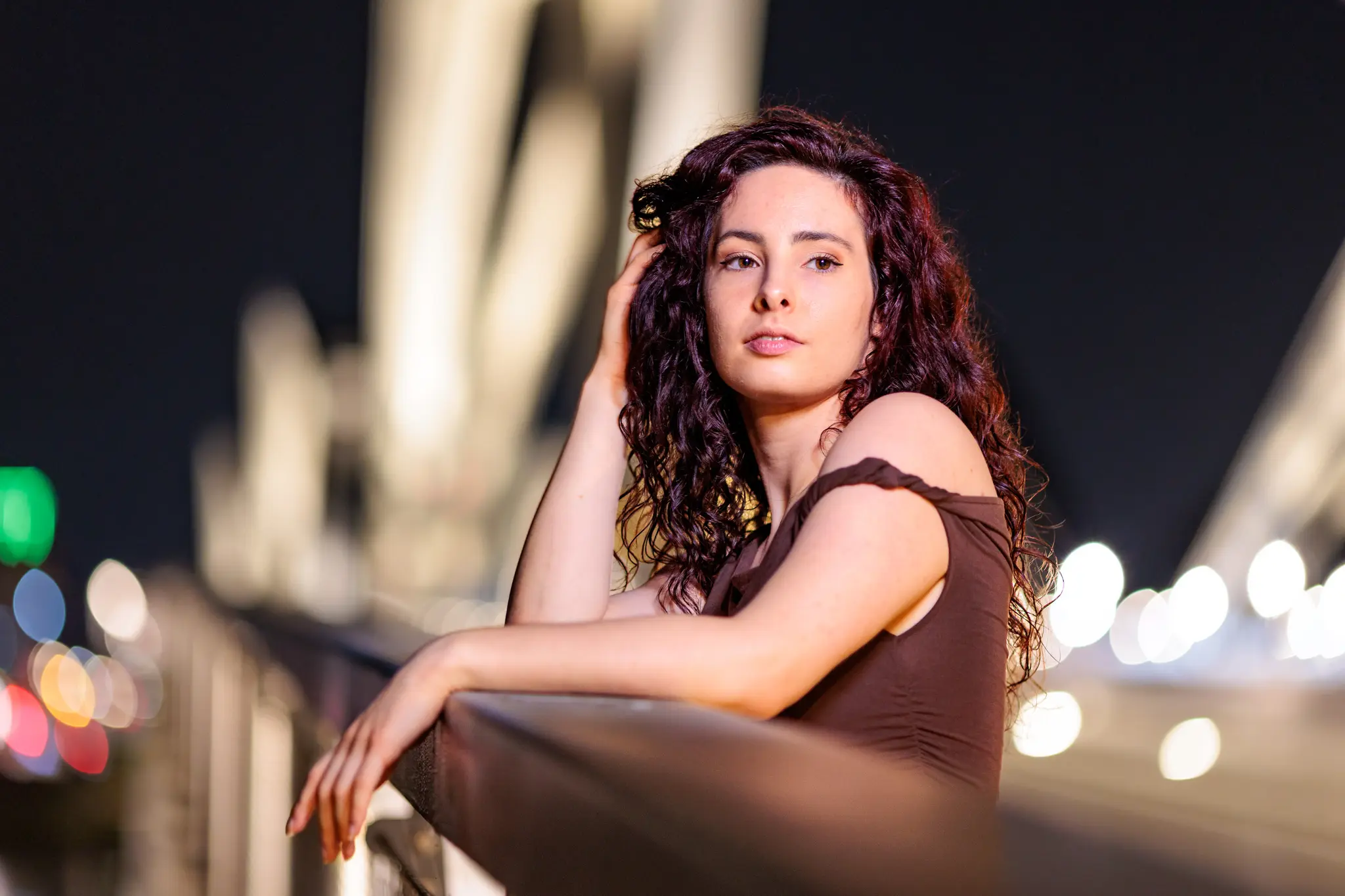 Porträt von Nicole mit dunklem, lockigem Haar, die bei Nacht auf der Linzer Eisenbahnbrücke anlehnt, im Hintergrund verschwimmen stimmungsvolle Stadtlichter