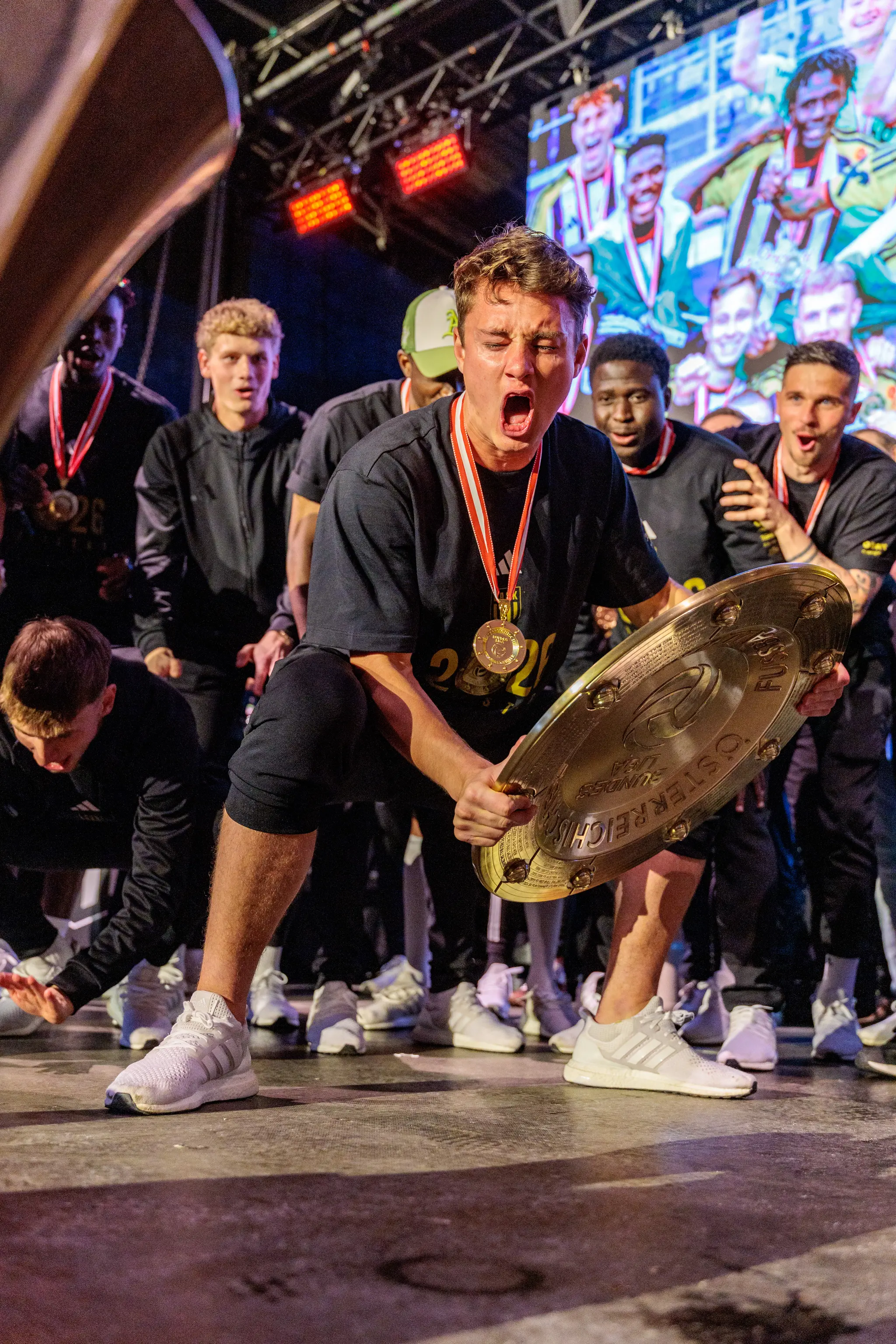 Ein LASK-Spieler hockt während der Meisterfeier in Linz und hält den Meisterteller voller Freude fest
