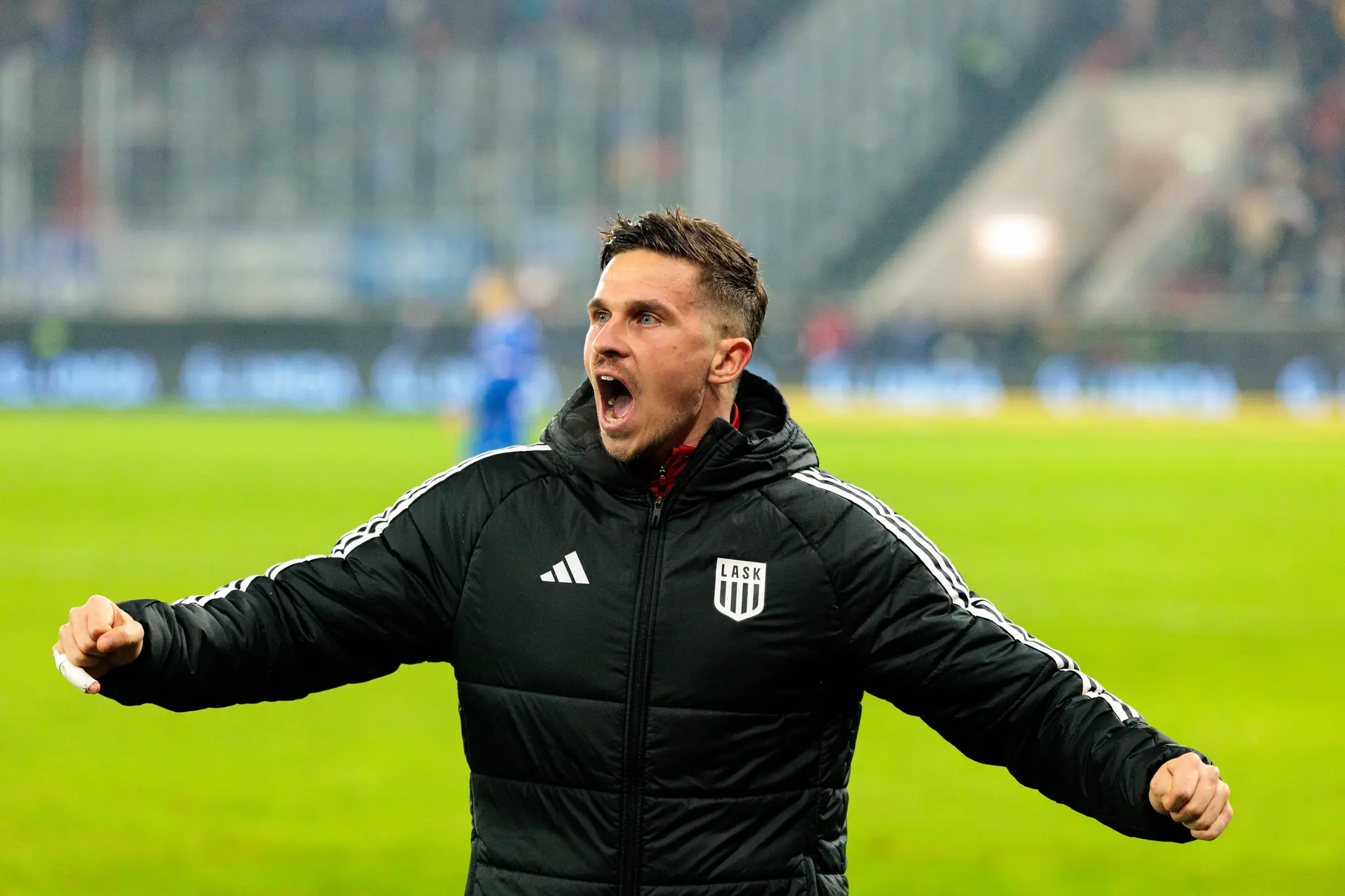 Ein emotional jubelnder LASK-Spieler in schwarzer Winterjacke feiert mit geballten Fäusten und lautem Schrei den Erfolg im Cup-Derby gegen Blau-Weiß Linz