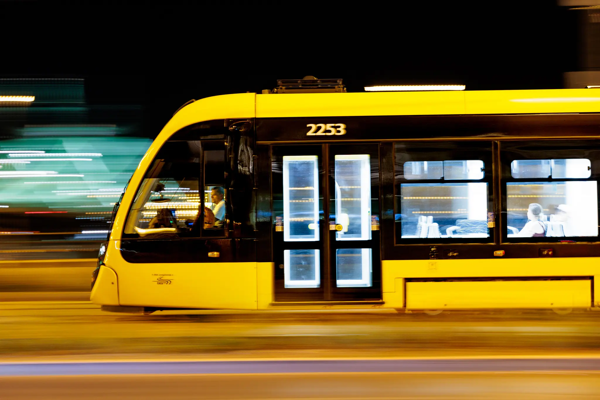Gelbe und schwarze Straßenbahn 2253 in Budapest. Mitzieher bei Nacht, mit unscharfem Hintergrund, Fahrer und Passagiere sichtbar, urbaner Nahverkehr.
