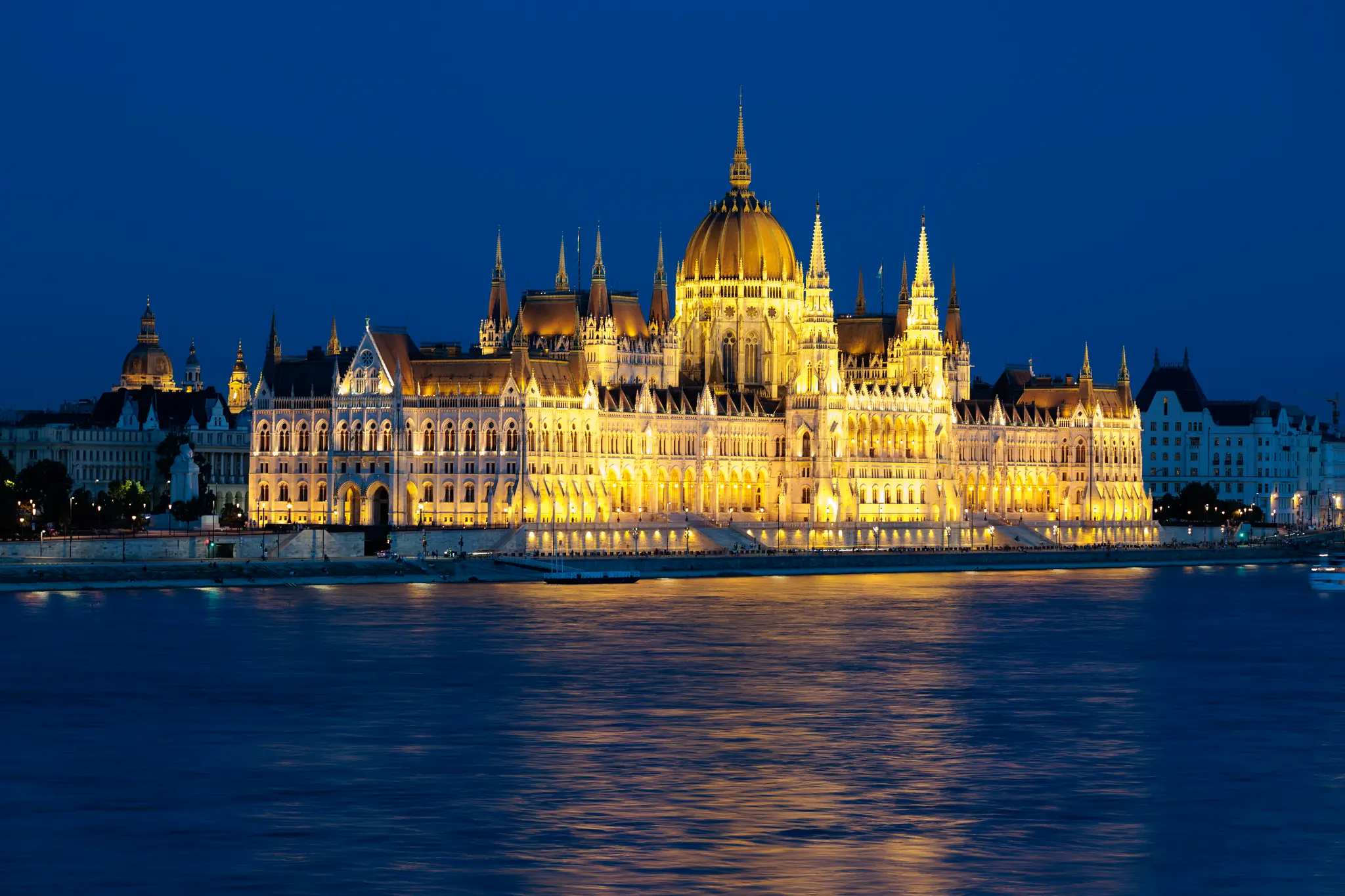 Nachtansicht des beleuchteten Ungarischen Parlamentsgebäudes in Budapest an der Donau, mit goldener Kuppel und hellen Lichtern, die sich im Wasser spiegeln. 