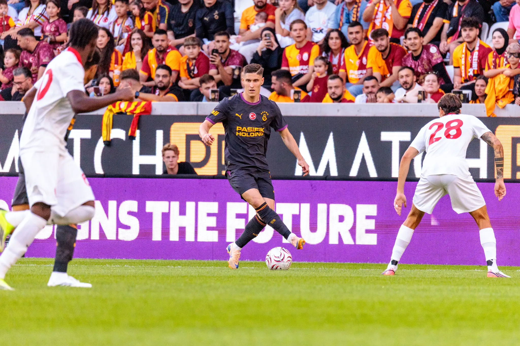 Galatasaray-Spieler dribbelt mit dem Ball, während Monza-Spieler Nummer 28 von rechts und Nummer 20 von links herannahen.