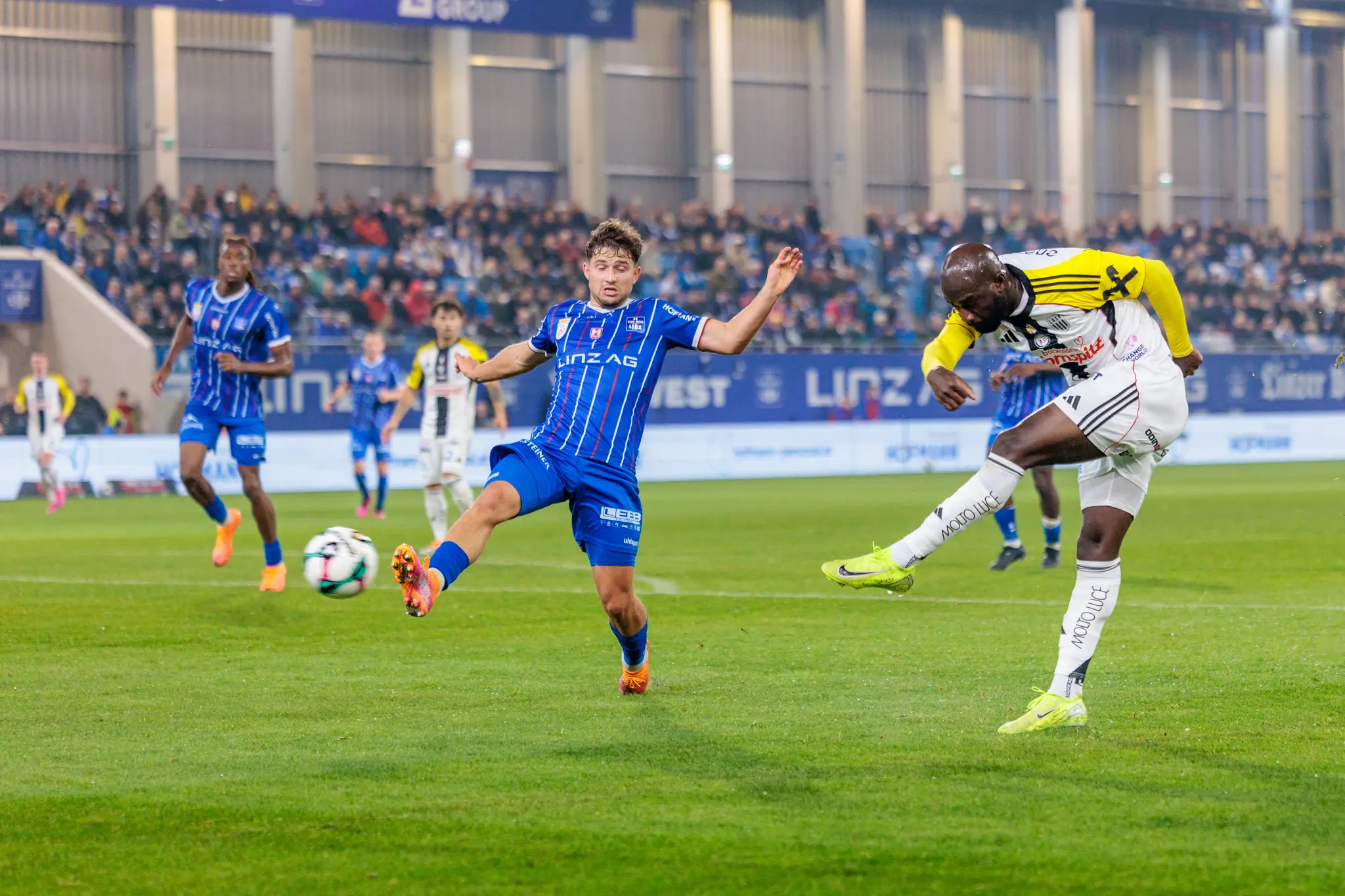 LASK-Spieler Moses Adeniran schießt den Ball mit energischem Einsatz auf das Tor, während ein Spieler von Blau-Weiß Linz daneben steht
