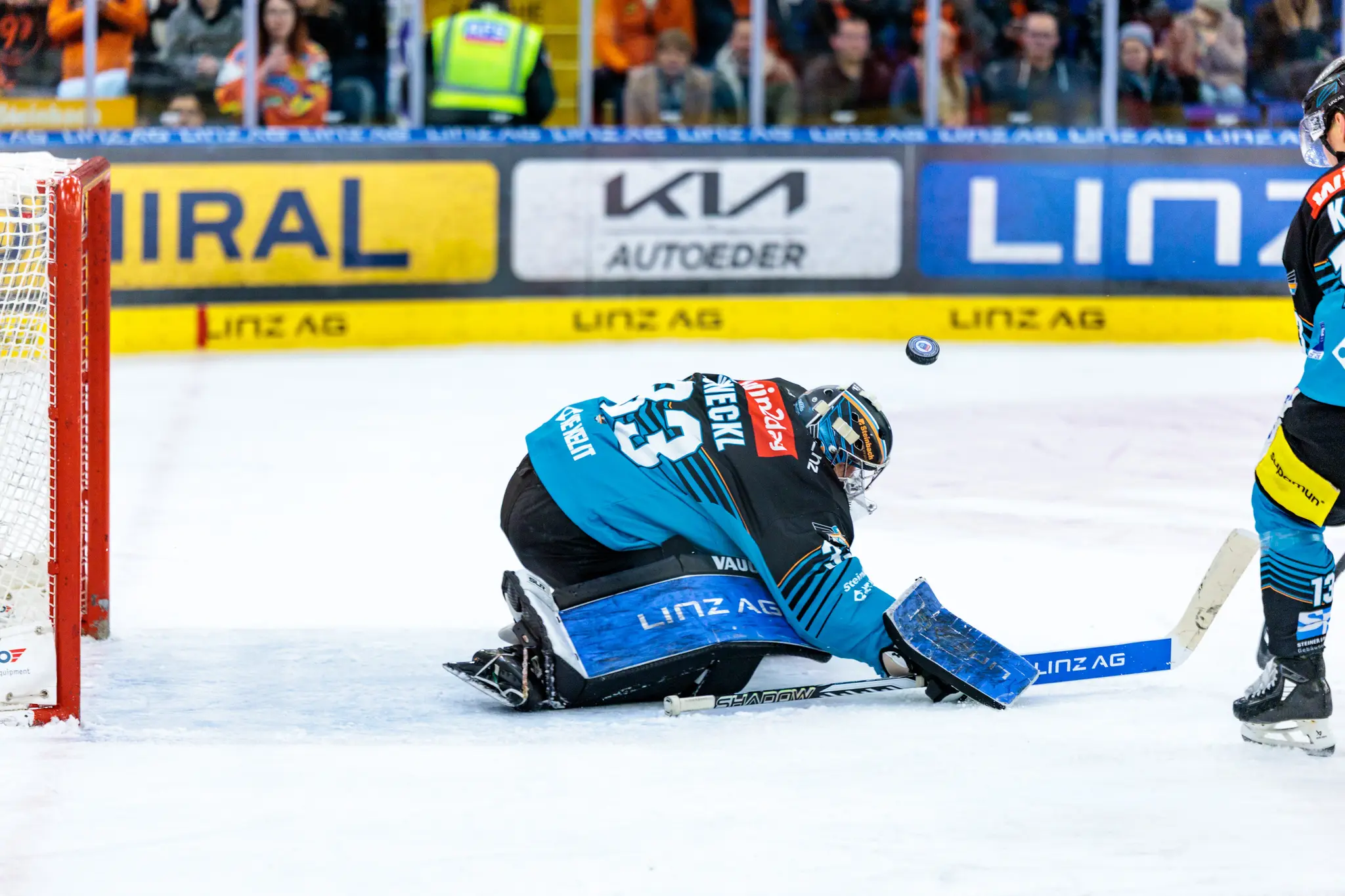 Eishockey-Torwart der Black Wings in teal-schwarzer Ausrüstung wehrt einen Puck ab, der knapp über seinem Helm fliegt