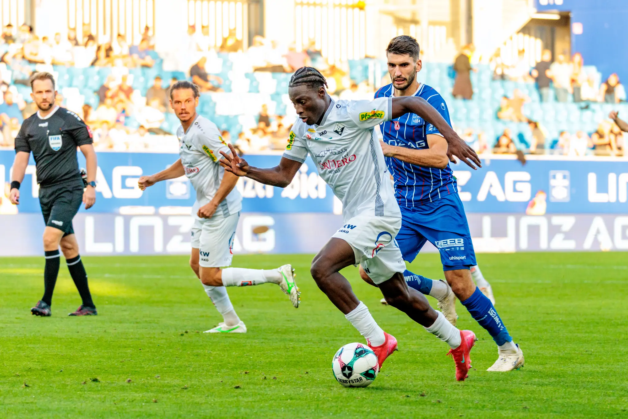 Der Altacher Spieler Ousmane Diawara in einem dynamischen Dribbling mit dem Ball, dicht verfolgt von einem Gegenspieler des FC Blau-Weiß Linz