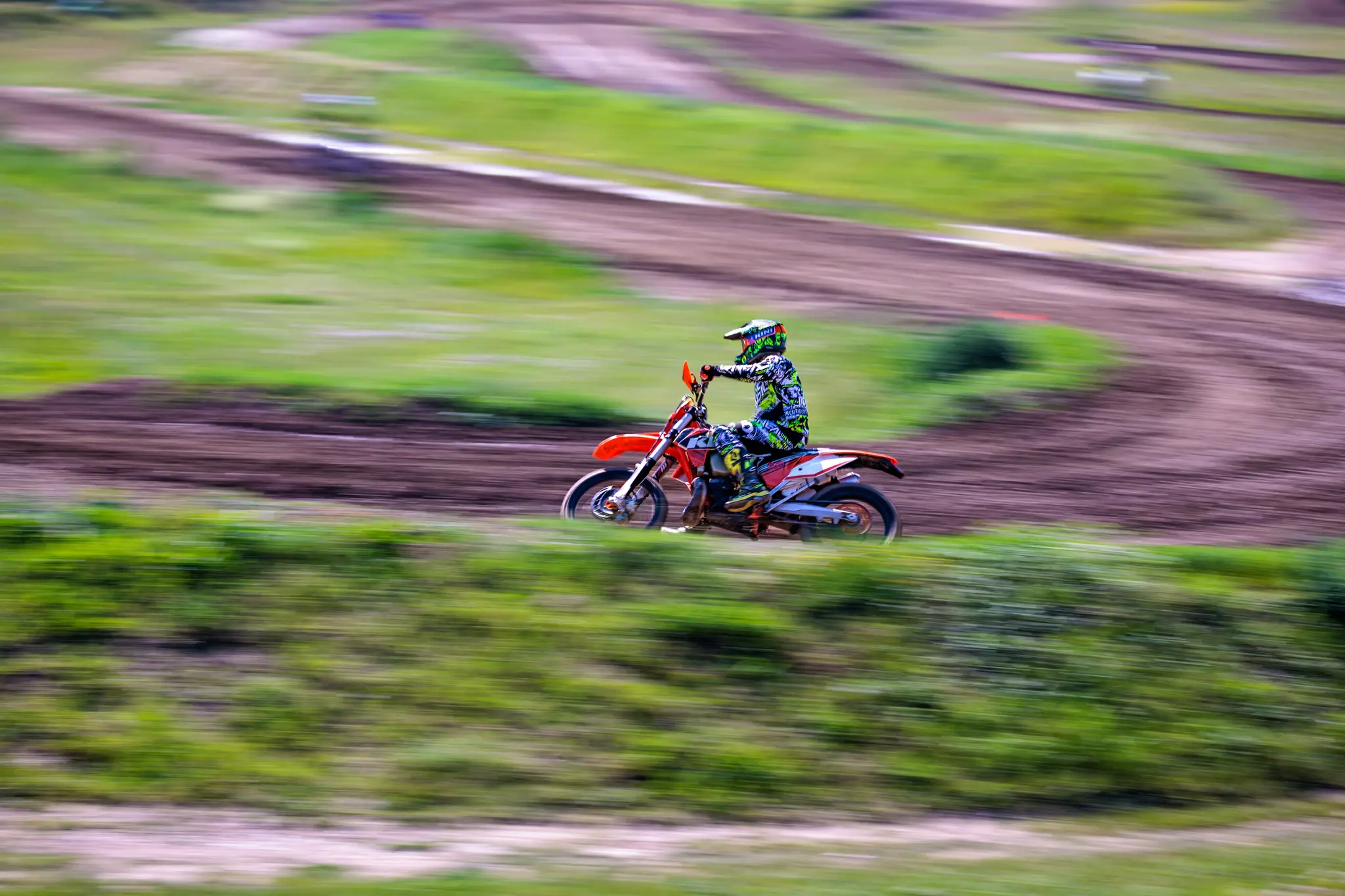 Mitzieher eines Motocrossfahrer in voller Fahrt auf orangefarbenem Dirt Bike auf einer Motocrossstrecke 