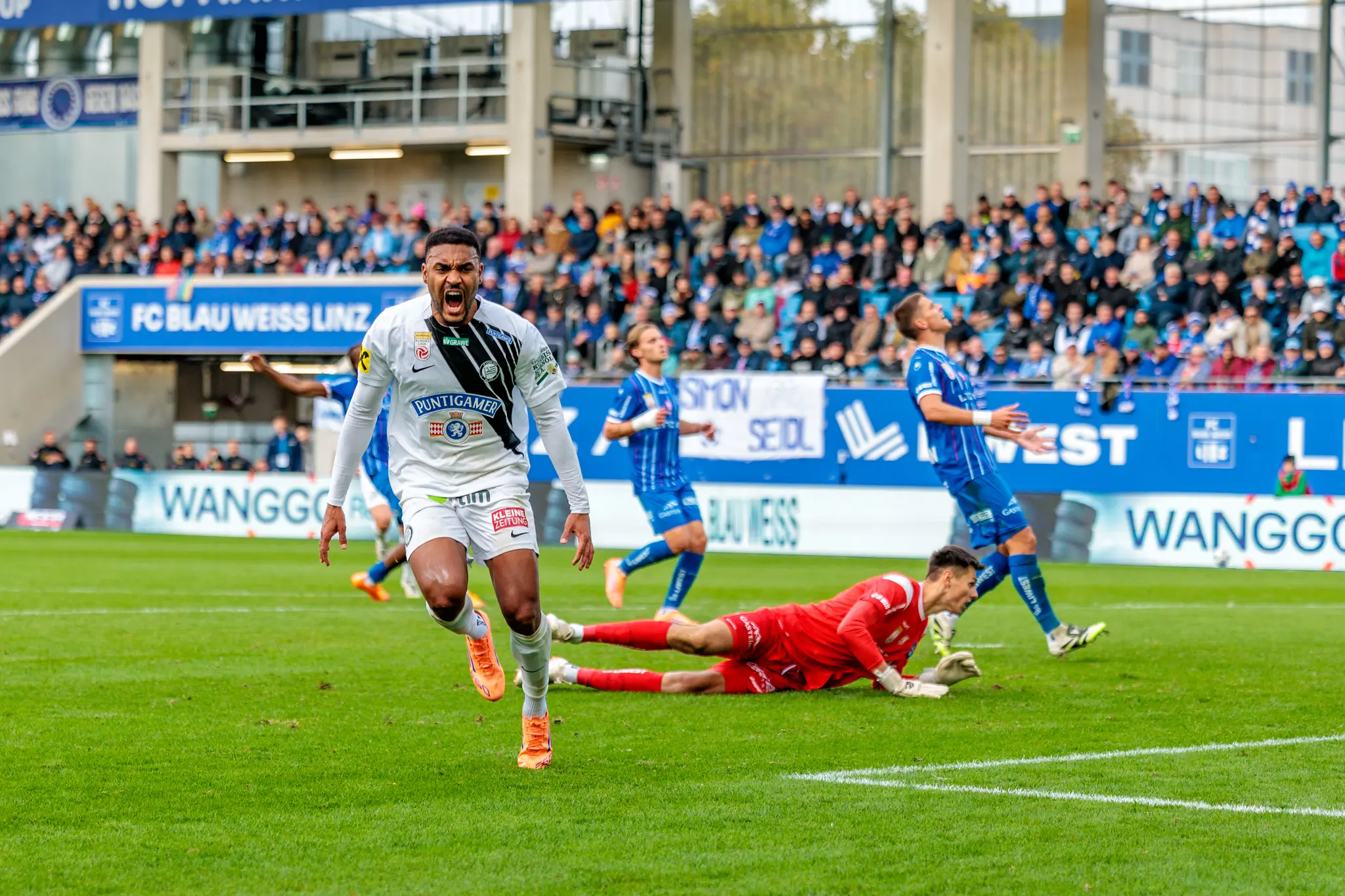 Sturm-Spieler Maurice Malone jubelt emotional über seinen Treffer gegen Blau-Weiß Linz, während der gegnerische Tormann geschlagen am Boden liegt